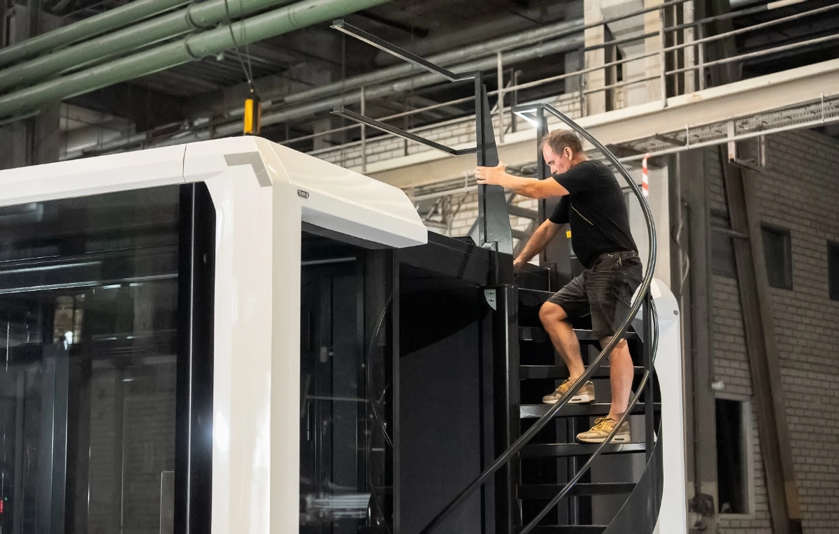 Technician climbing a spiral staircase to the rooftop of an Expandable relocatable unit during assembly inside a production facility