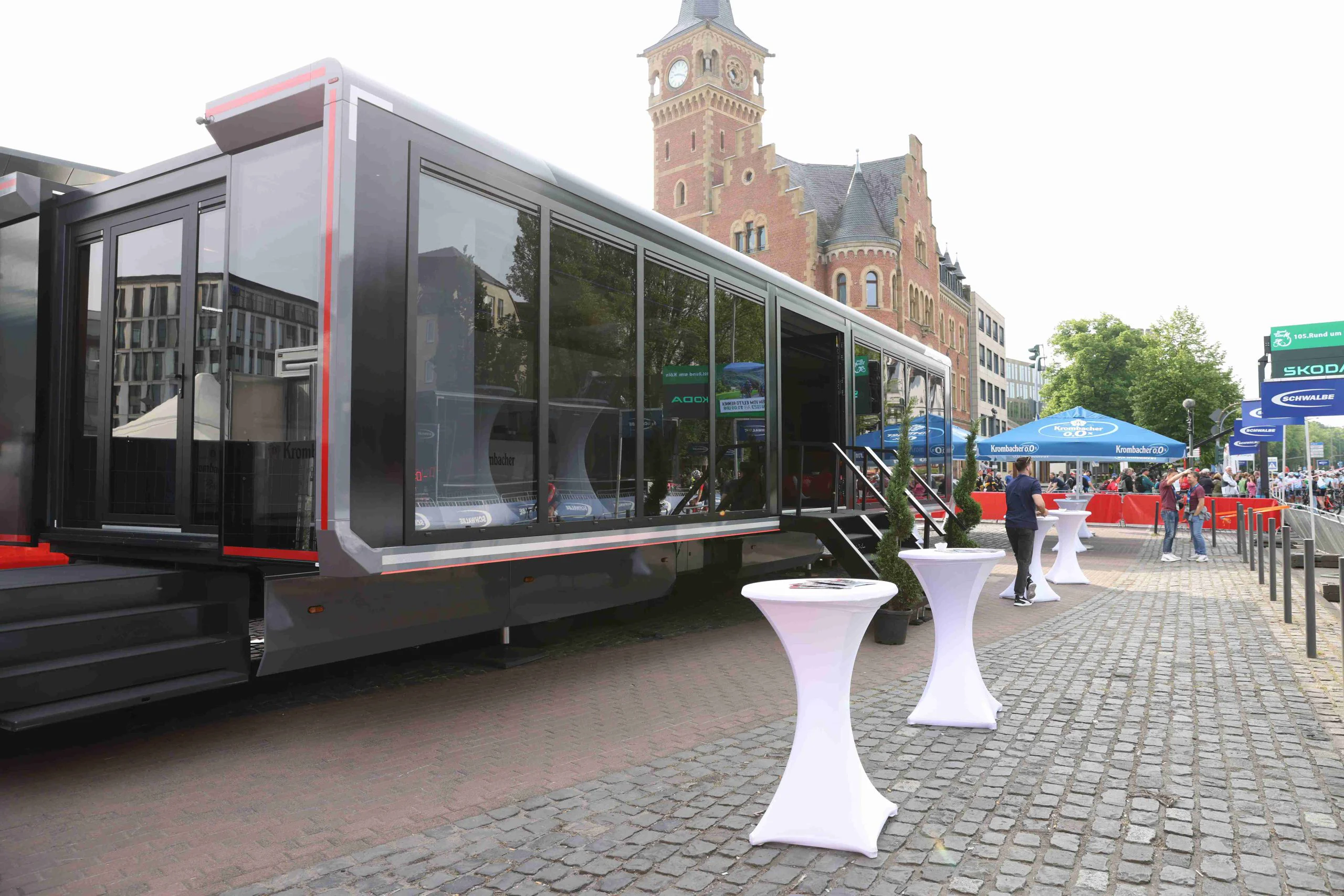 Expandable trailer deployed at an outdoor event, showcasing its spacious, fully extended interior with large glass windows, set against a historic brick building backdrop.