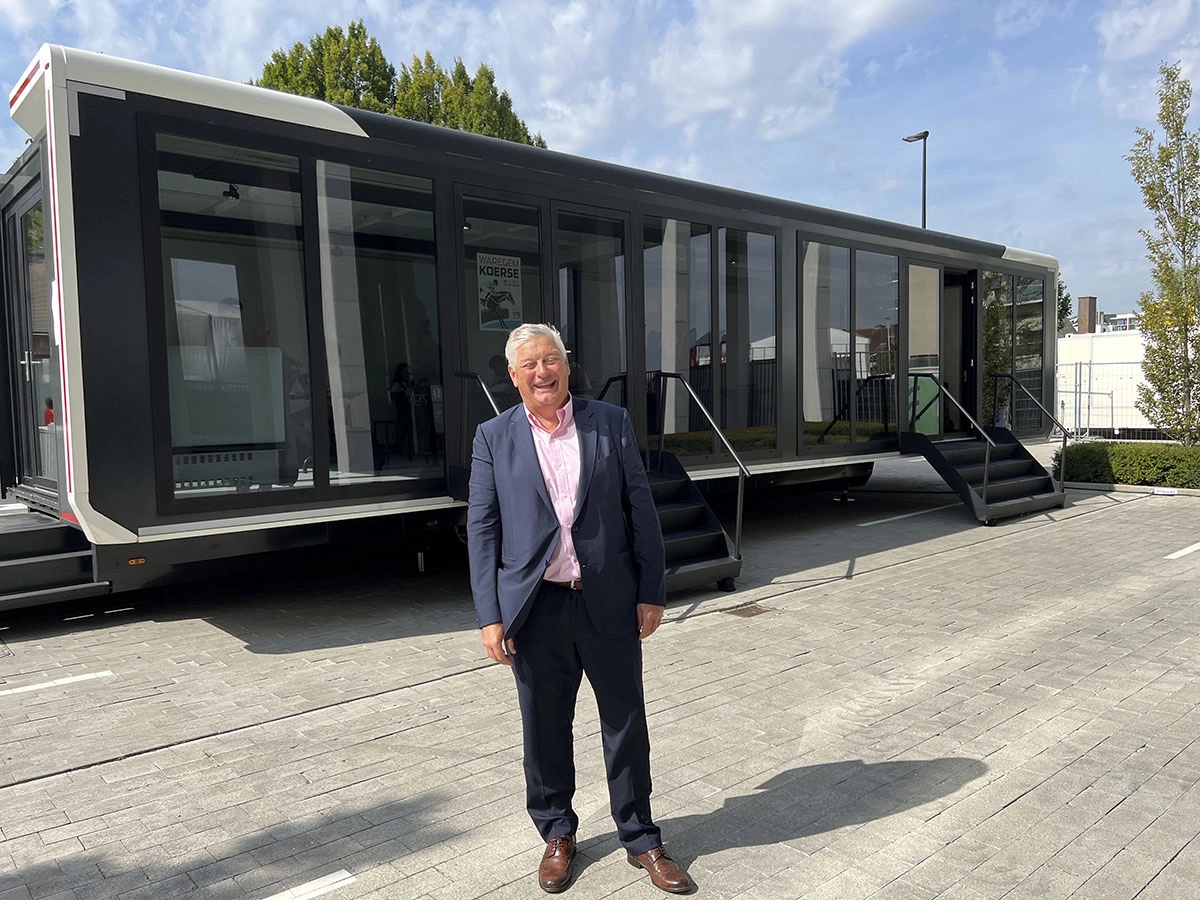 Smiling Serge Blommaert in business attire standing in front of a fully extended, modern Expandable trailer with large glass windows at an outdoor event
