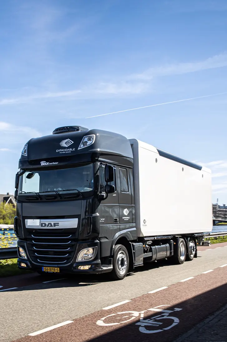 A black DAF truck with an expandable emergency response trailer moving along a clear road under a blue sky