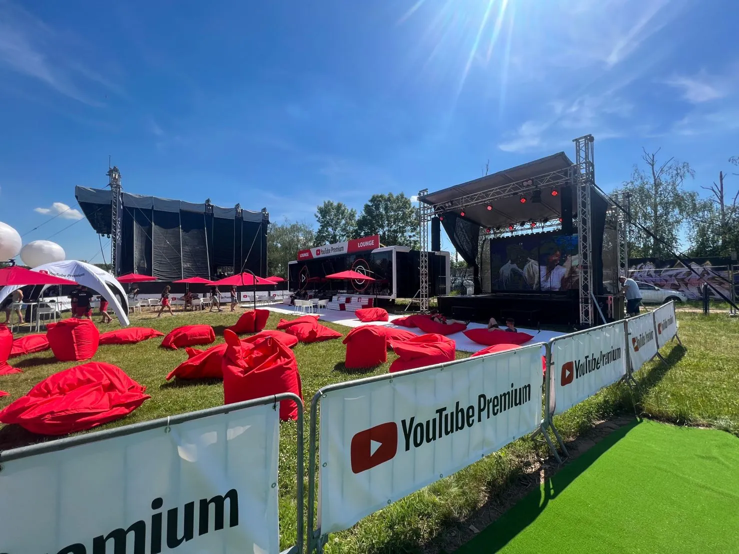 Ein Event-Trailer an einem Veranstaltungsort im Freien mit dem Logo âYouTube Premiumâ, umgeben von roten SitzsĂ€cken und Sonnenschirmen, unter klarem blauem Himmel