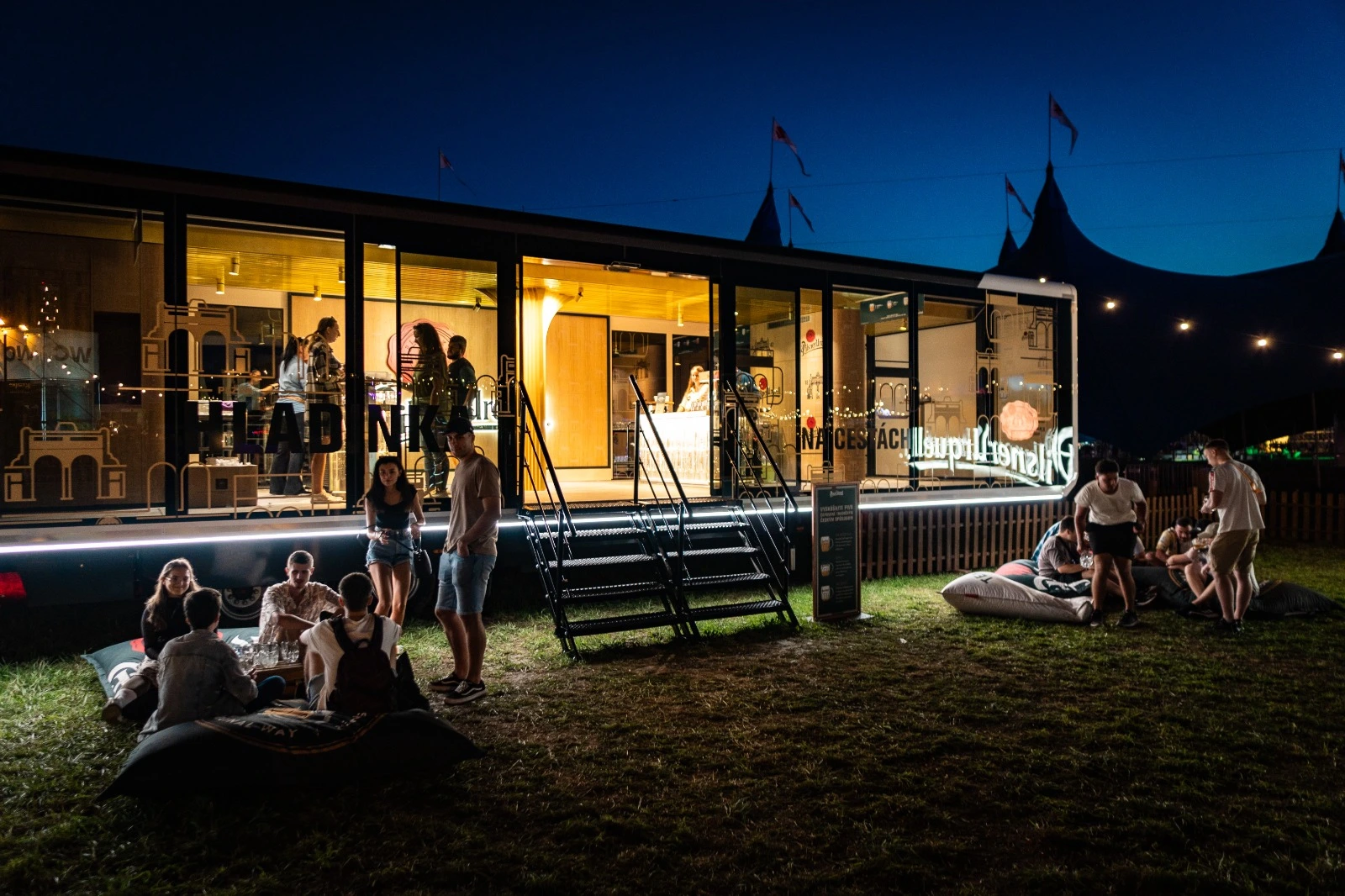 Evening shot of a promotional trailer with a vibrant atmosphere as festival-goers relax on bean bags.