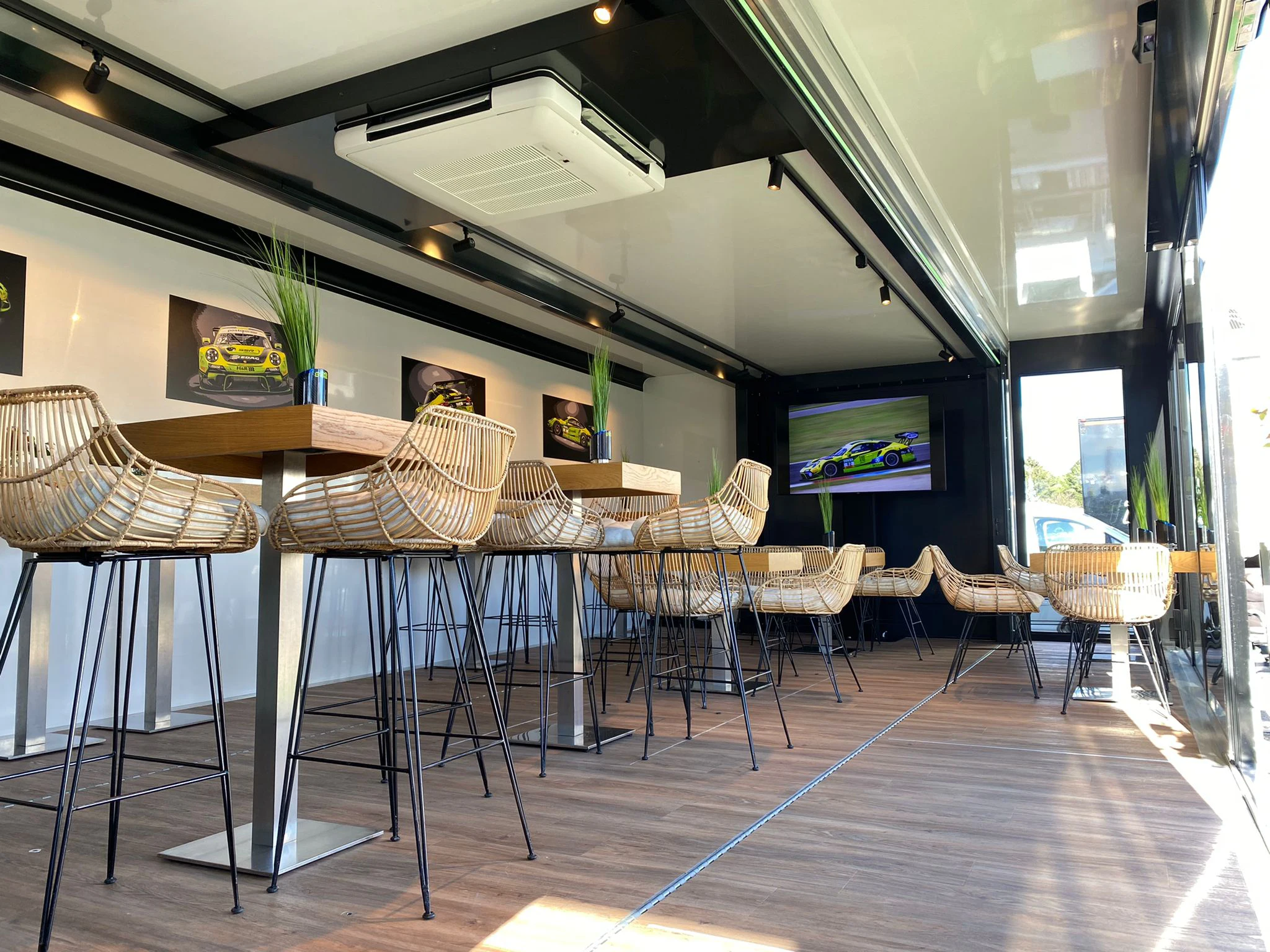 A sleek interior of a mobile food trailer with high-top rattan chairs, a bar setup showcasing images of race cars, and a bright, airy atmosphere