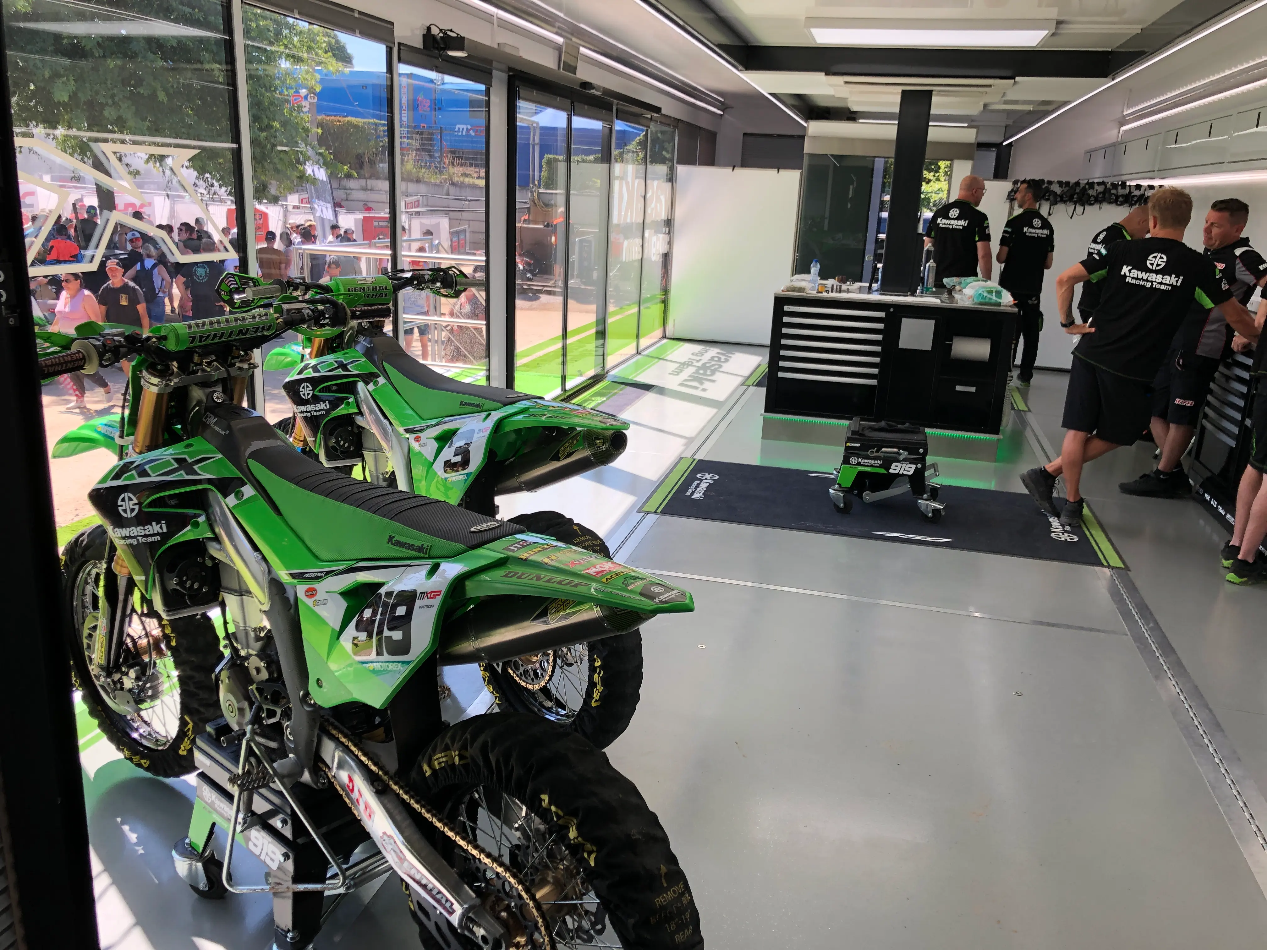 Inside the Expandable Motorcycle trailer with green motorcycles inside and a team of engineers around the green motorcycles