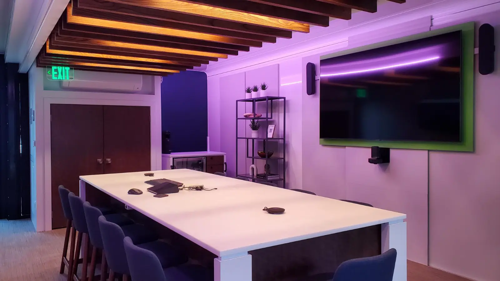 Innenraum eines erweiterbaren mobilen Sicherheitsanhängers, der einen Besprechungsbereich mit einem langen weißen Tisch, violetter Umgebungsbeleuchtung und montierten digitalen Bildschirmen zeigt.