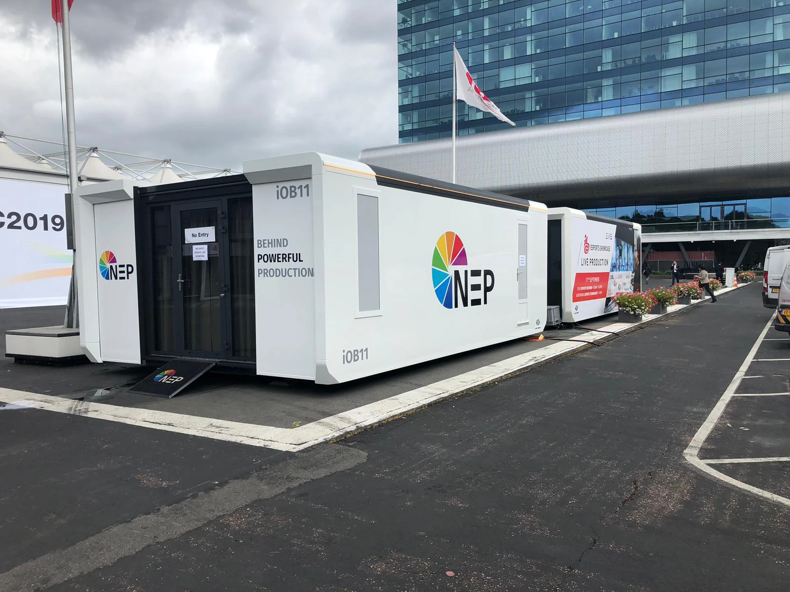 Exterior view of a NEP mobile control room trailer parked at an event location, with branding that reads 'BEHIND POWERFUL PRODUCTION,' highlighting its role in live broadcast productions