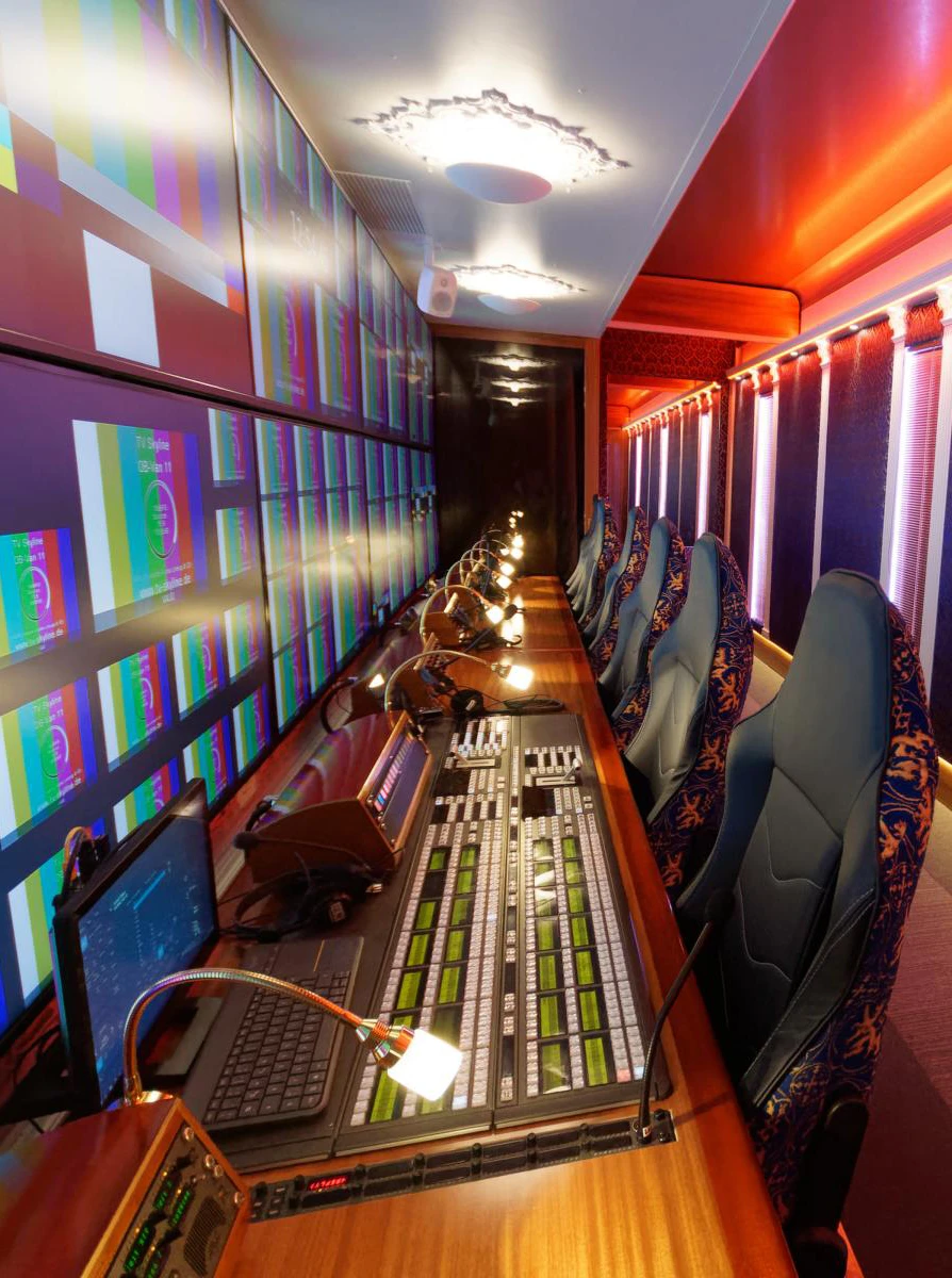 Interior of a mobile control room designed for live production, featuring a long mixing console with multiple monitors in a vibrant red and purple-lit setting.