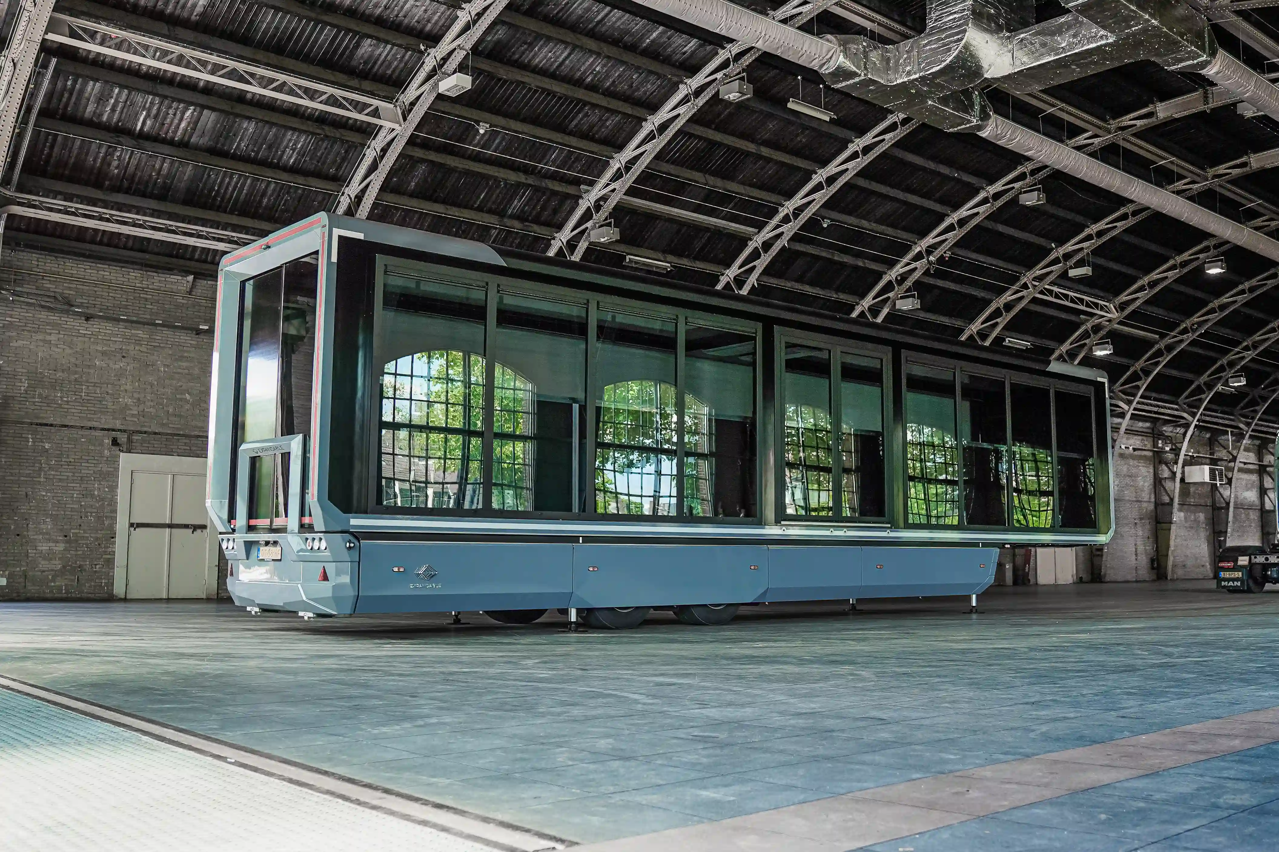 Ein Mobile Fotostudio in einem gerÀumigen Wohnwagen mit einem langen Arbeitsplatz mit Computern und Monitoren unter blauem Umgebungslicht vor dem Hintergrund einer Skyline der Stadt.