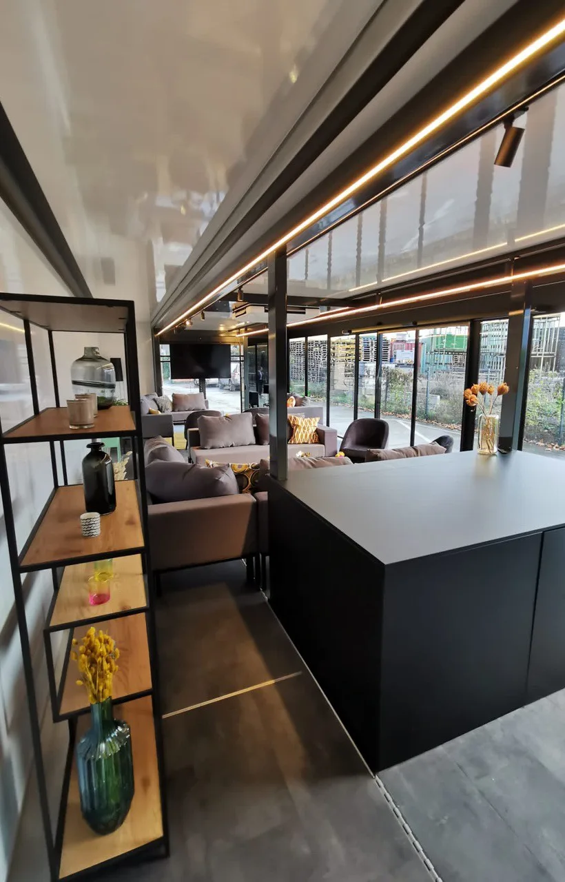 Interior of a mobile office trailer designed as a cozy office space with modern furniture, wooden shelves, ambient lighting, and large windows offering natural light