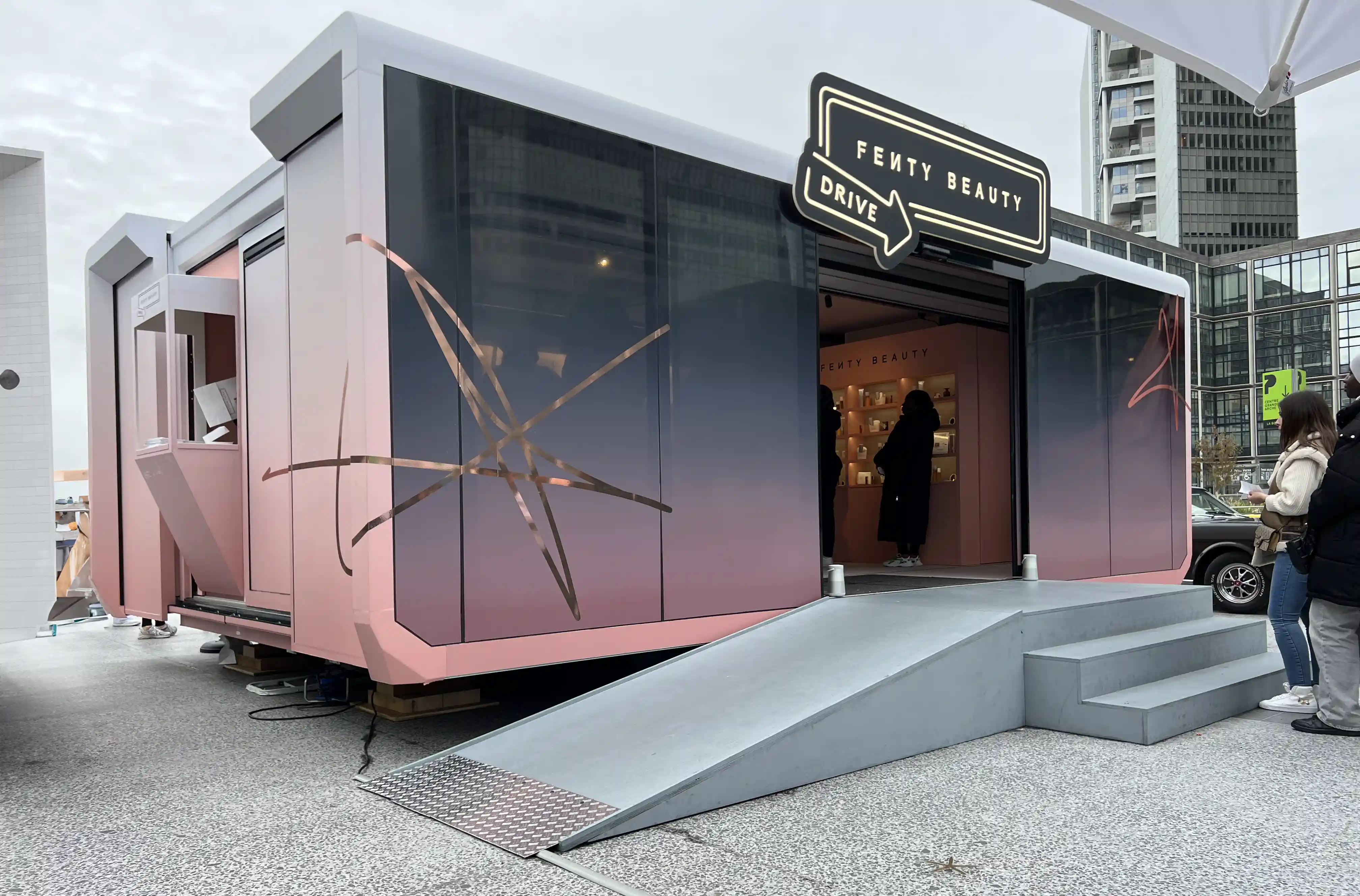 Un camión itinerante de la marca ABB estacionado frente a un edificio moderno con una llamativa escultura azul en el césped. El cielo está nublado, lo que crea un espectacular telón de fondo para este espacio móvil emergente, lo que deja entrever su potencial para funcionar en diferentes condiciones meteorológicas y entornos.