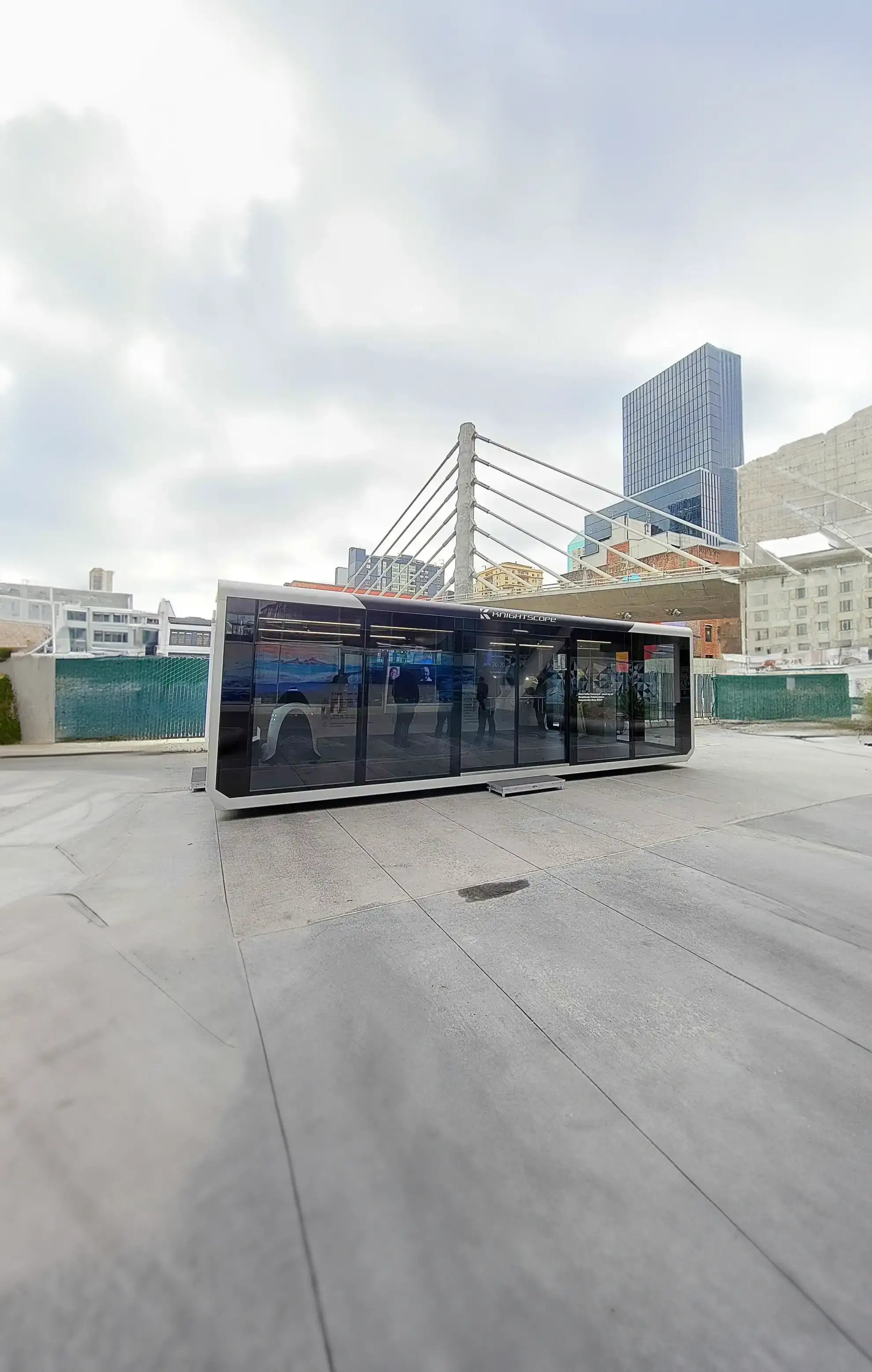 Ein mobiler Sicherheitsanhänger von Expandable, der in einer urbanen Umgebung mit Wolkenkratzern im Hintergrund positioniert ist. Es verfügt über ein modernes Design mit reflektierenden Glasscheiben und einem eleganten schwarzen Rahmen.