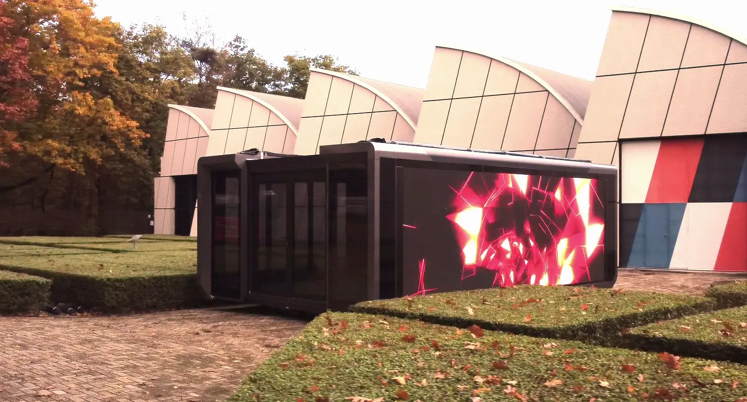Moderna unidad modular ampliable con una vibrante pantalla LED en contraste con un edificio artístico y un follaje otoñal, que ejemplifica la tecnología de eventos de vanguardia.