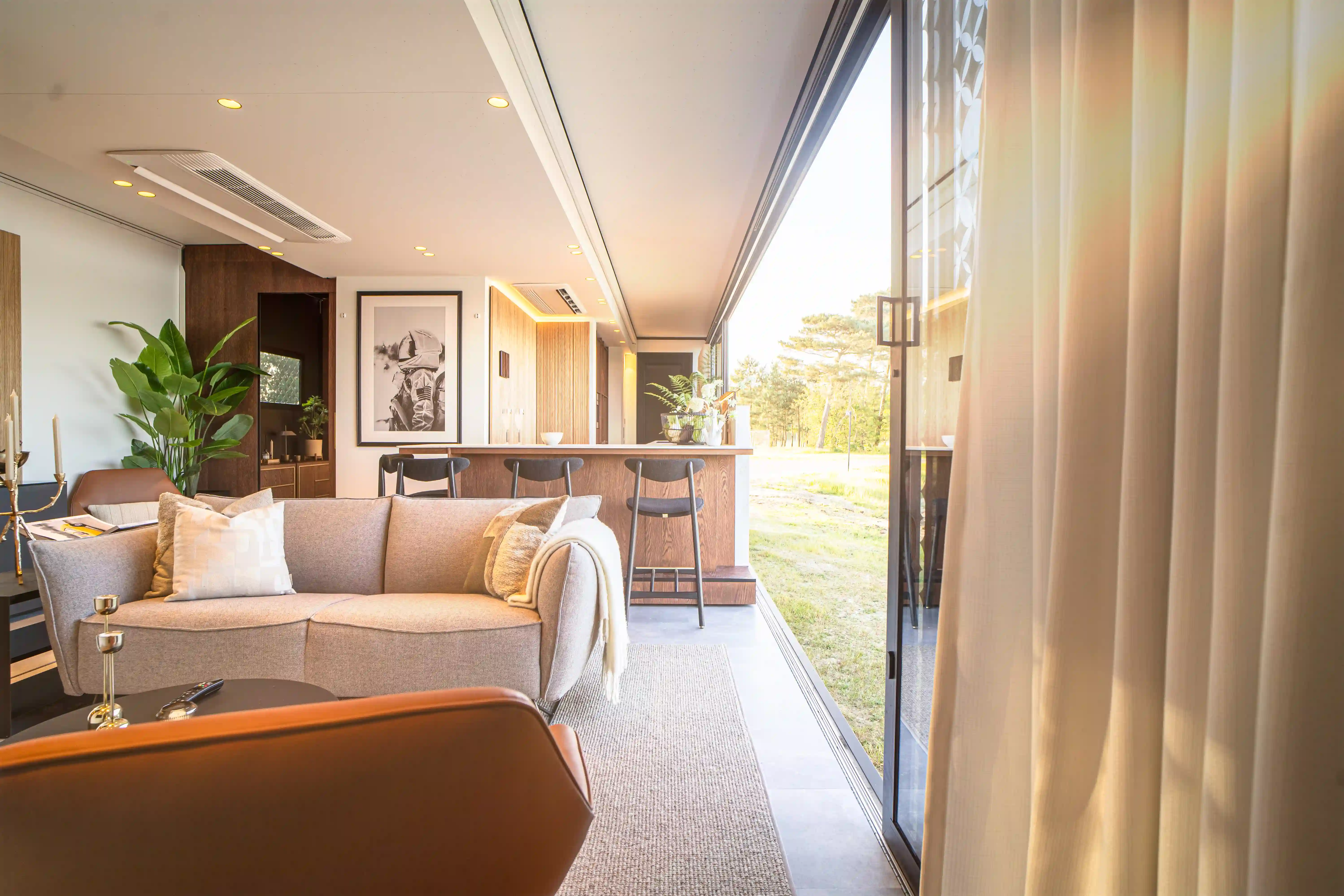 A spacious and well-lit living area inside an expandable mansion, featuring comfortable seating, modern decor, and large glass doors that open to a scenic outdoor view.