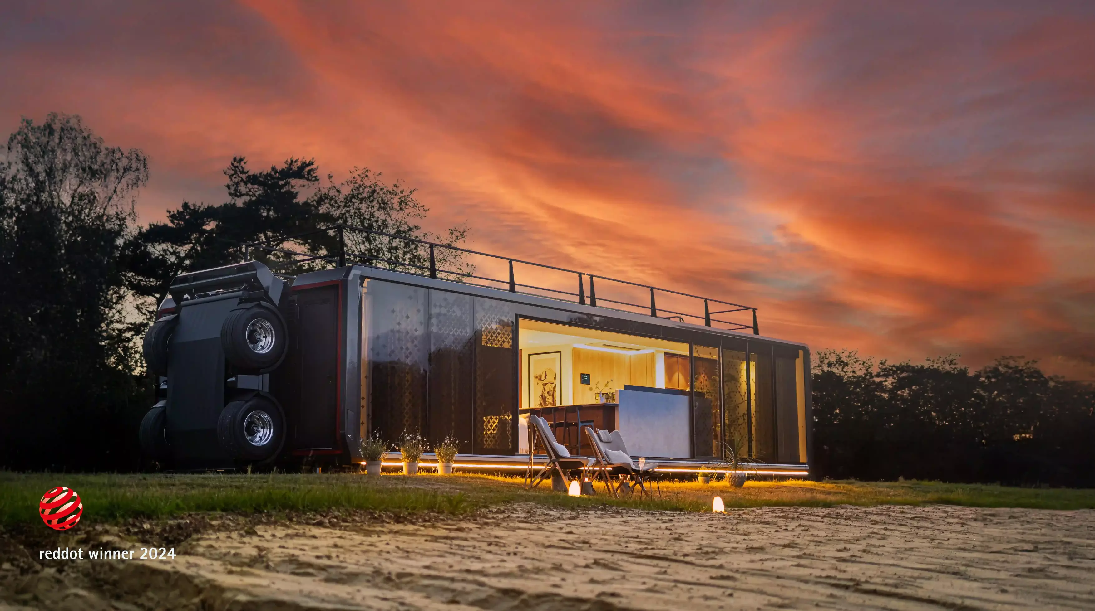 Expandable Mansion at sunset, showcasing a luxurious mobile home with glass panels and modern interior, set against a scenic outdoor backdrop with a colorful sky.