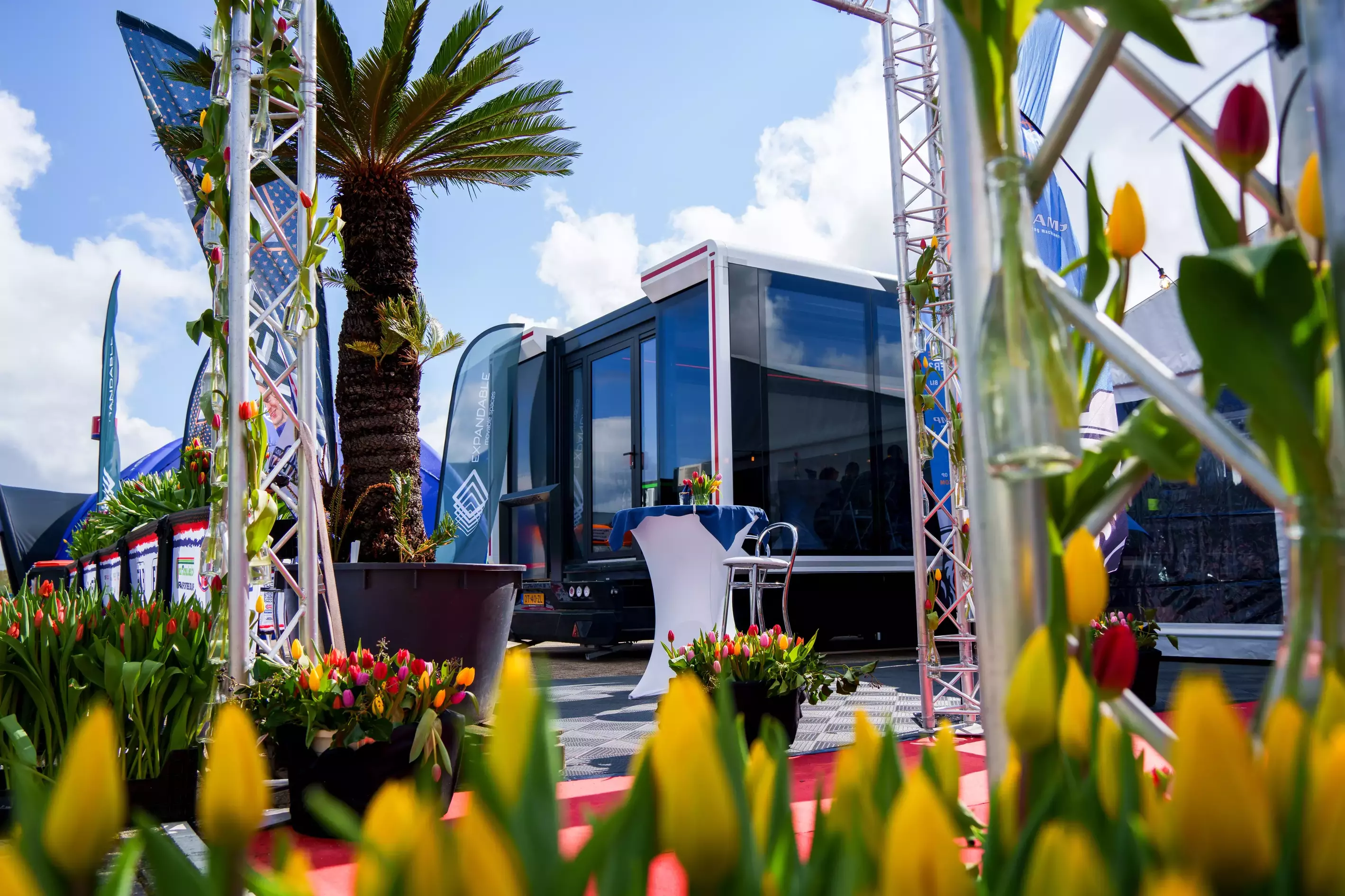 The Expandable hybrid hospitality trailer is parked on a paved area next to a building, showing its reflective glass facade and extendable side sections for increased space.