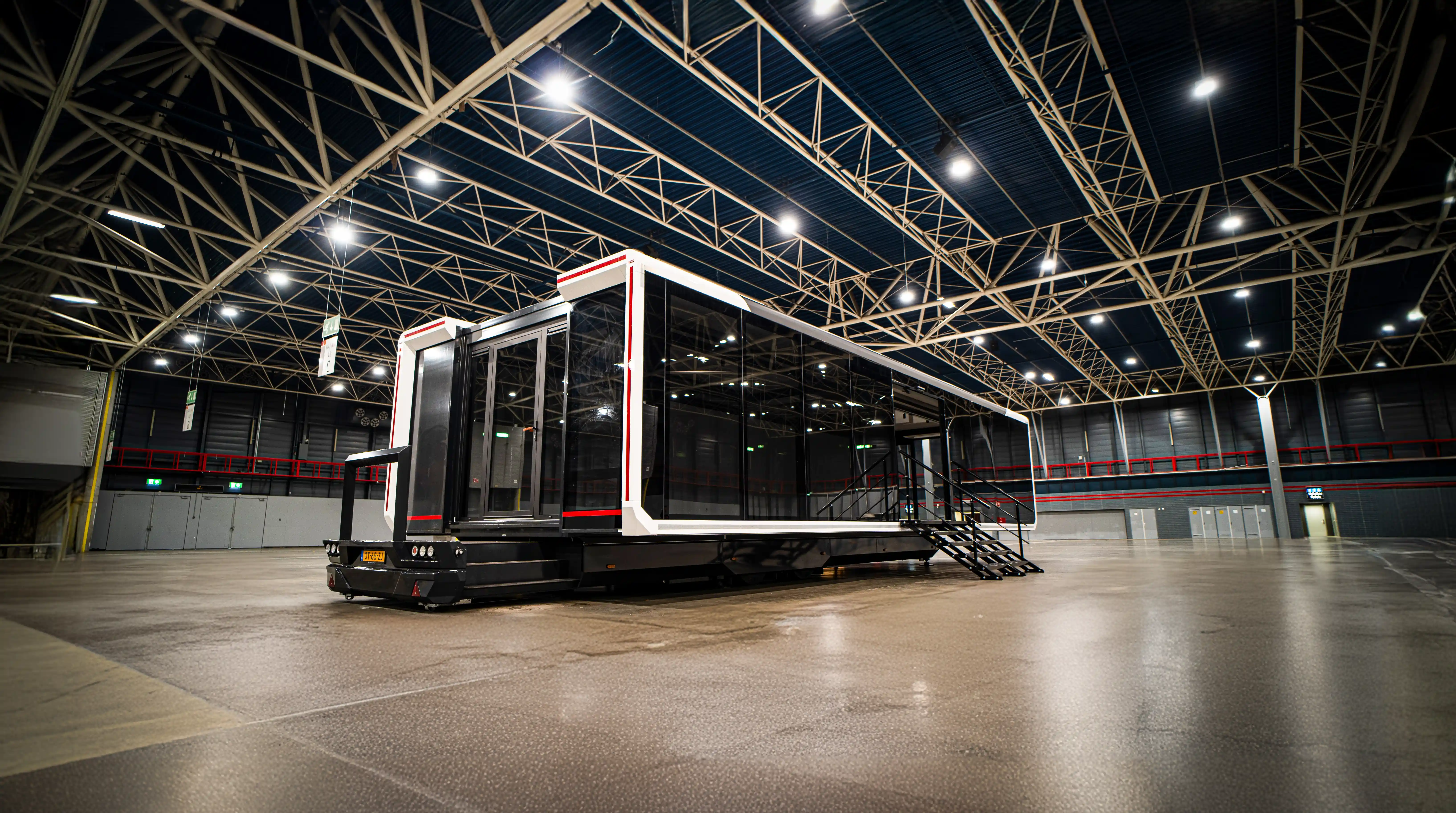 Expandable mobile trailer set up inside a spacious indoor facility. The sleek, modern structure features large glass windows and black and white exterior panels with red accents. 