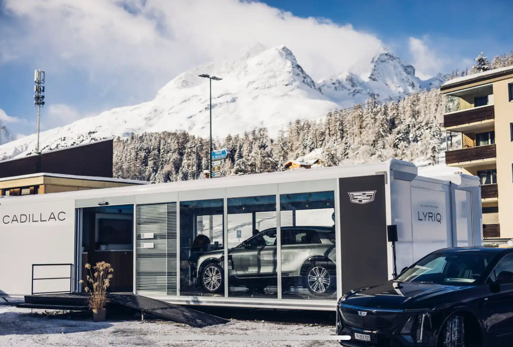 Vertikaler Blick auf einen Anhänger eines Autohauses mit einem ausgestellten Luxusauto, das von natürlichem Licht durchflutet wird, das durch die großen Glasfenster fällt, vor einer ruhigen Kulisse im Freien.