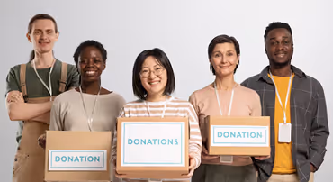 Five diverse volunteers smiling and holding boxes labeled Donation or Donations for a charity drive.