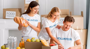 Three volunteers sorting and packing food items including bread and bottled drinks in a food donation center.