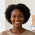 Smiling woman with curly hair wearing a brown top against a light background.