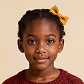 Portrait of a young girl with a yellow hair bow and burgundy top against a brown background.