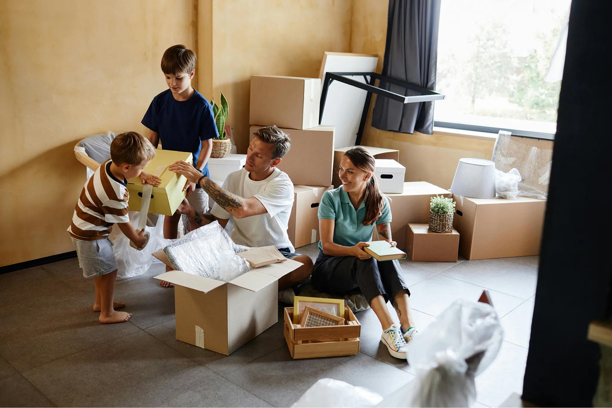 Family of four unpacking moving boxes in a room with cardboard boxes and household items.