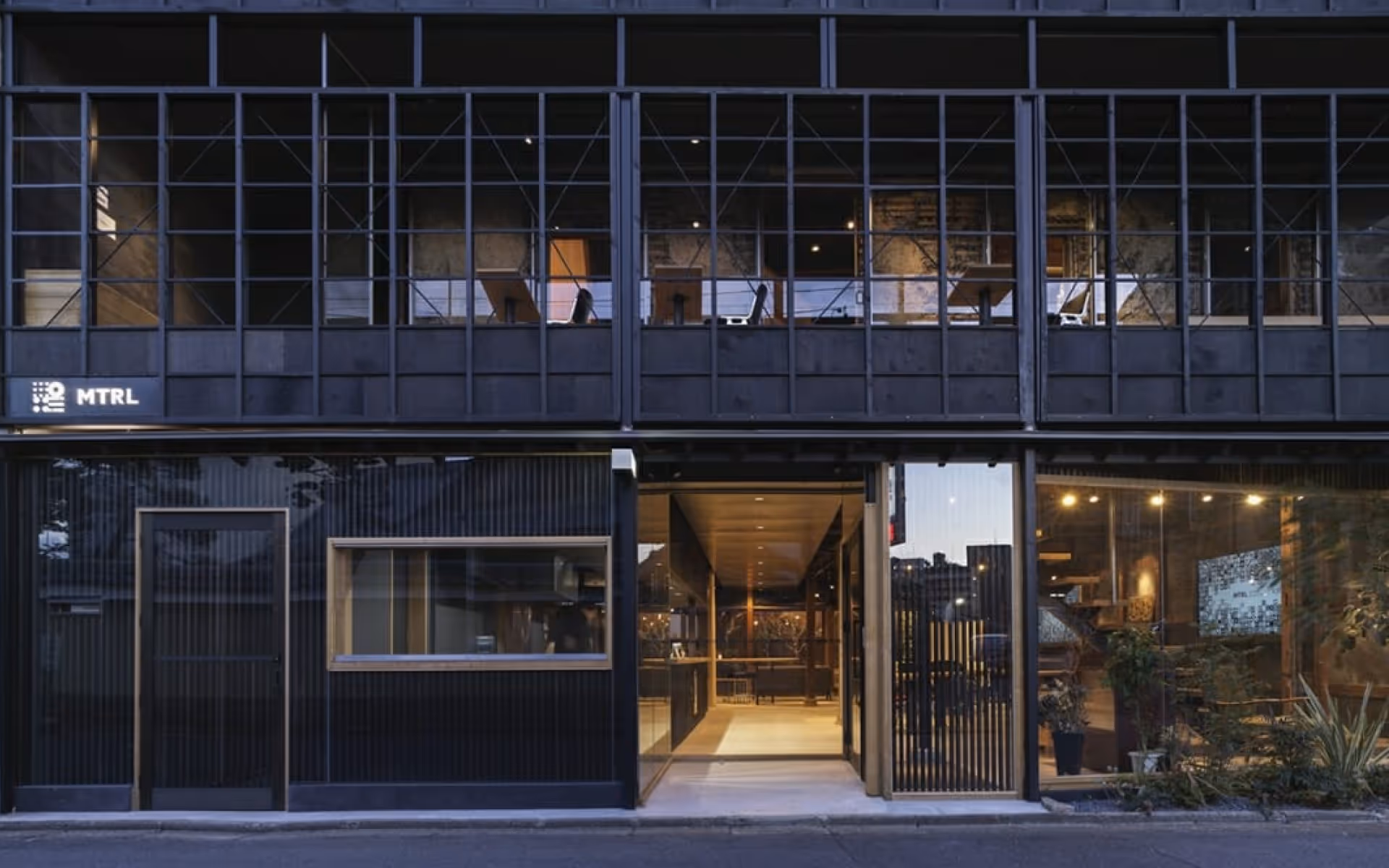 Exterior view of FabCafe Kyoto featuring a modern black façade, large windows, and softly lit interior.