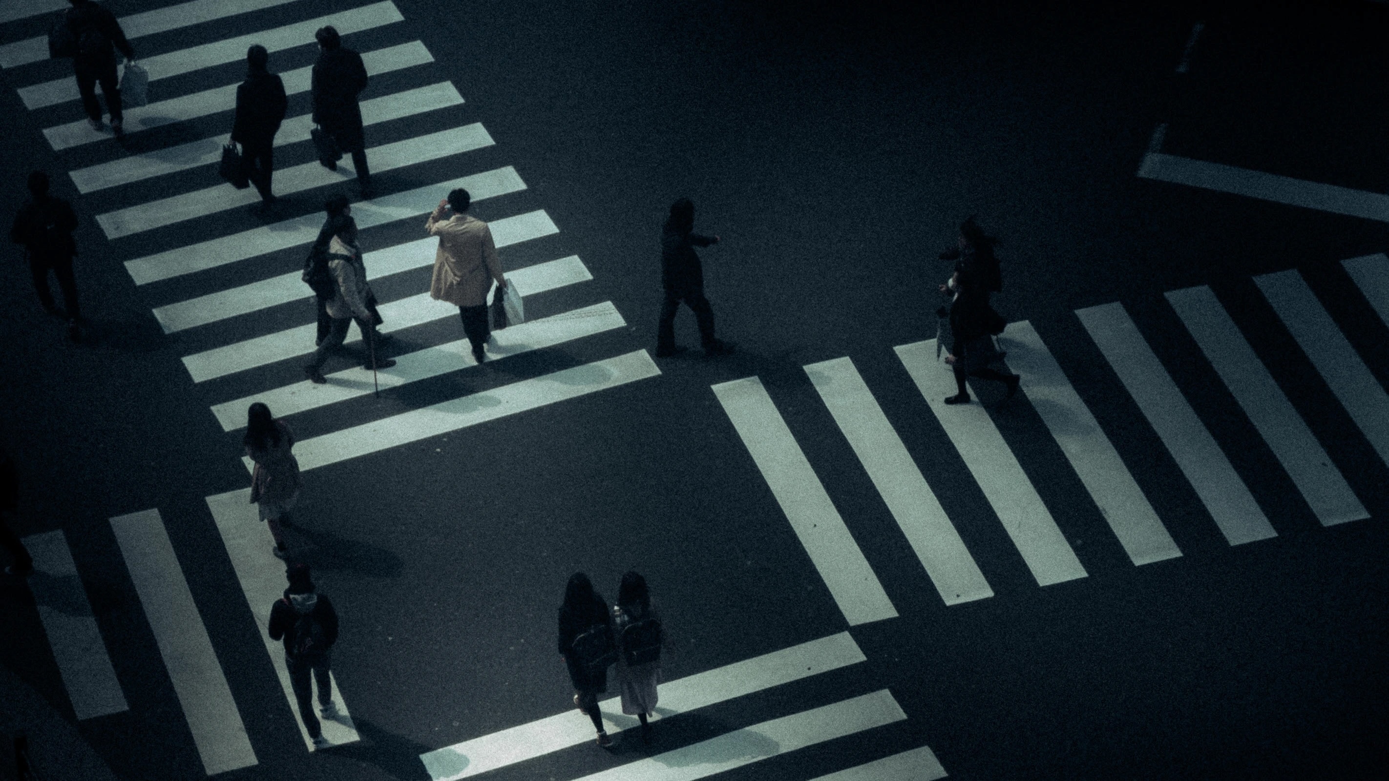 Overhead view of people crossing multiple intersecting pedestrian crosswalks in dim lighting.