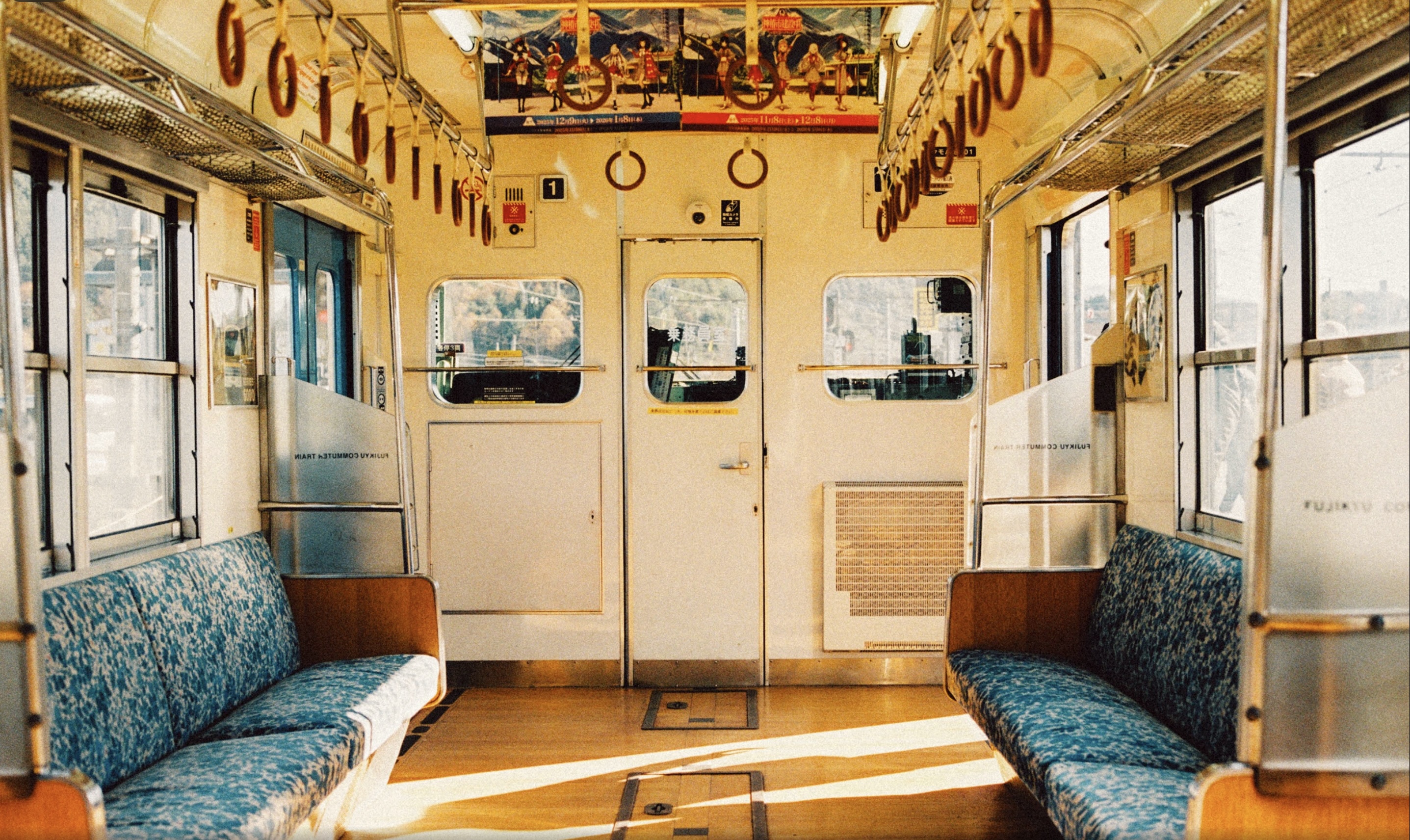 Empty train car interior with rows of blue patterned seats and hanging hand straps.