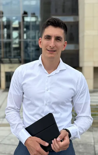 Muž v bílé košili stojící venku před budovou drží černé pouzdro na tablet.