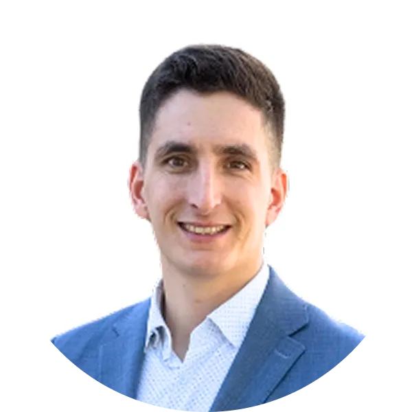 Mladý muž s krátkými tmavými vlasy v modrém saku a bílé košili s úsměvem na bílém pozadí.