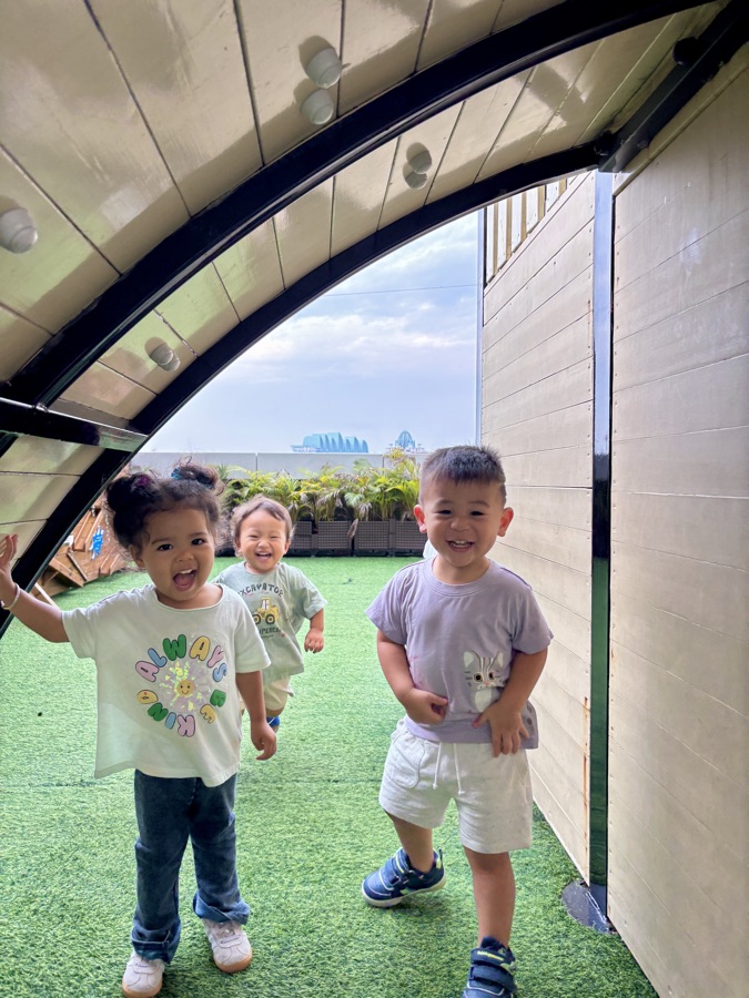 A small group of toddlers walking together across the rooftop garden.