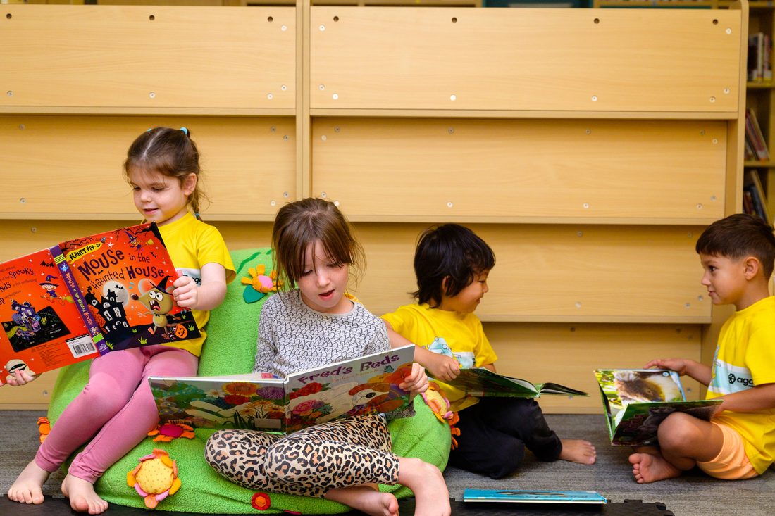 An educator reading a picture book to four children sitting on the library floor around her.