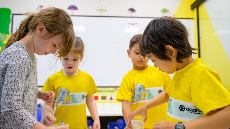 Four children gathered around a tray, all looking down at the cups as they work.