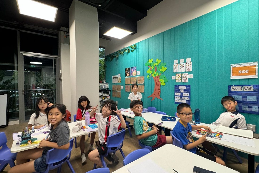 Children working at desks in a new classroom with a deep teal wall and a painted tree display.