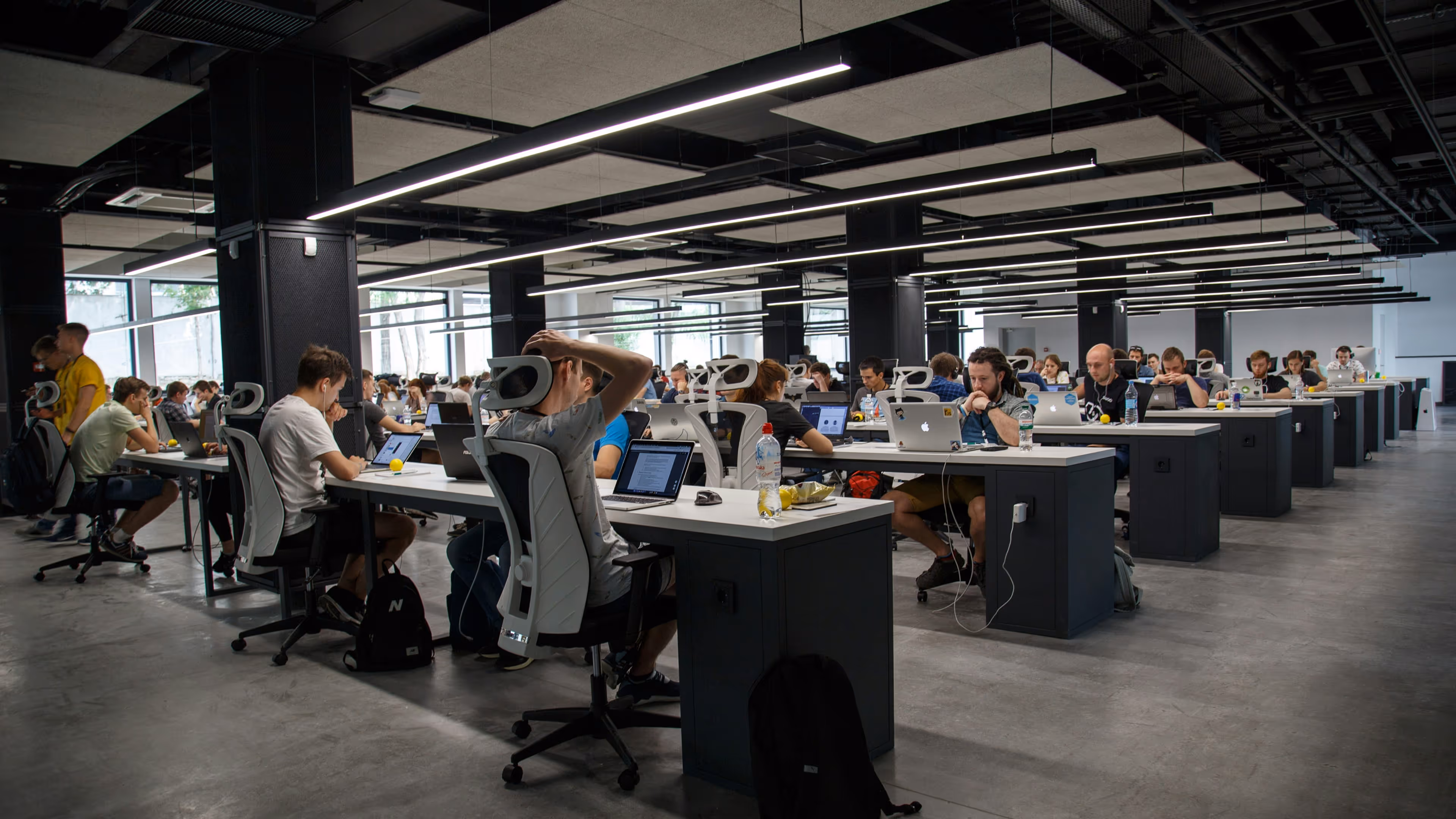 Open office space with multiple rows of desks where young people work on laptops.