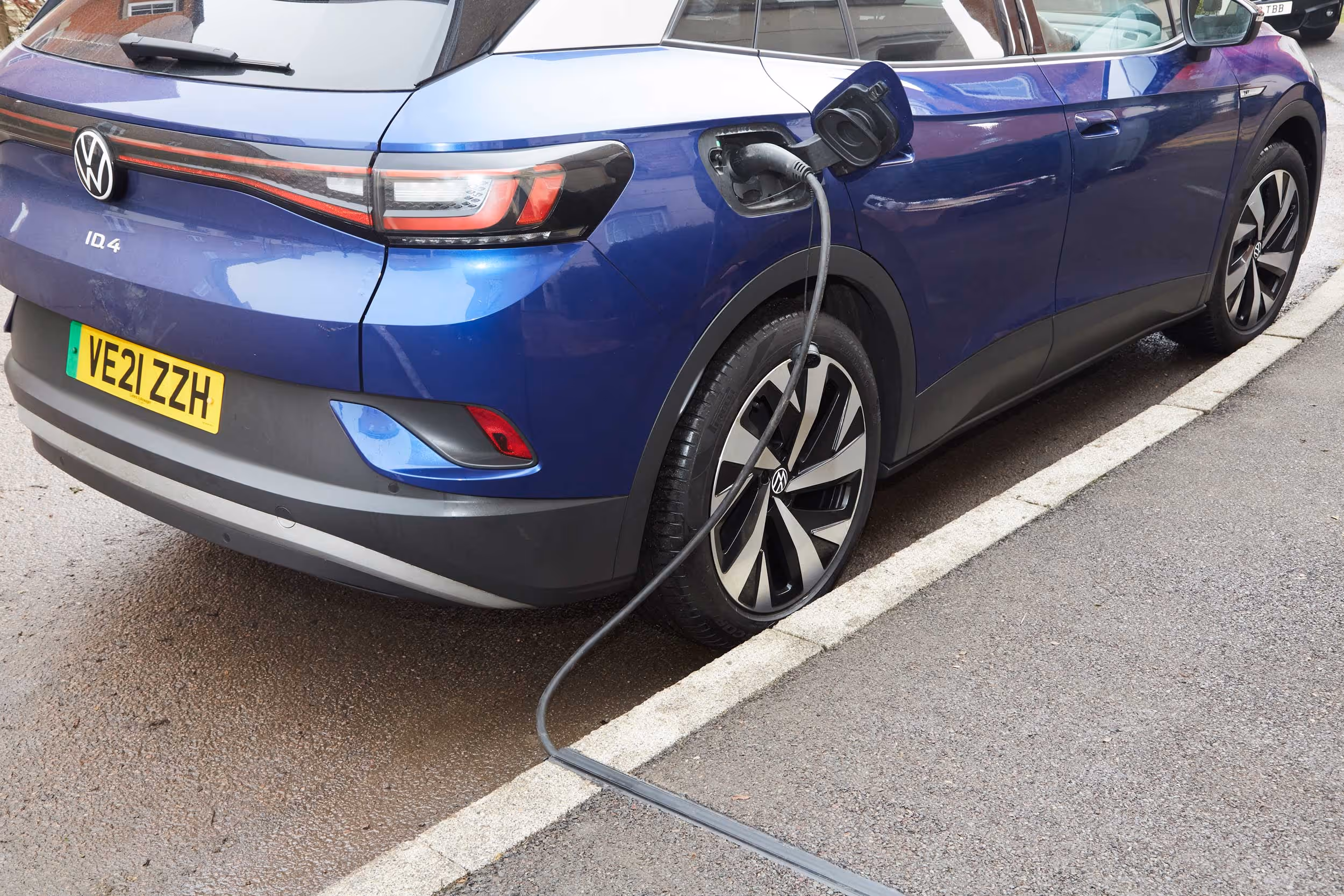 A blue electric car is parked on the street, plugged into a charging station.