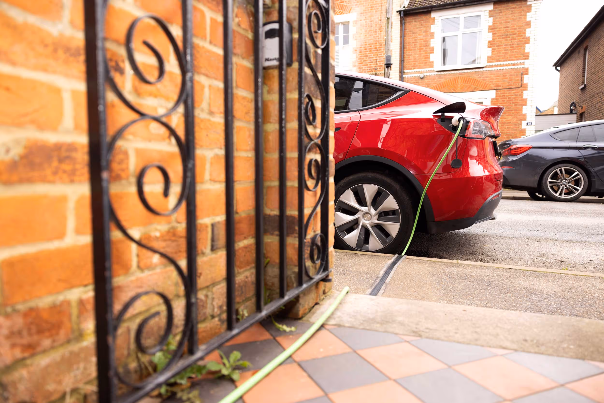 A red electric car is charging on a driveway with a visible charging cable.
