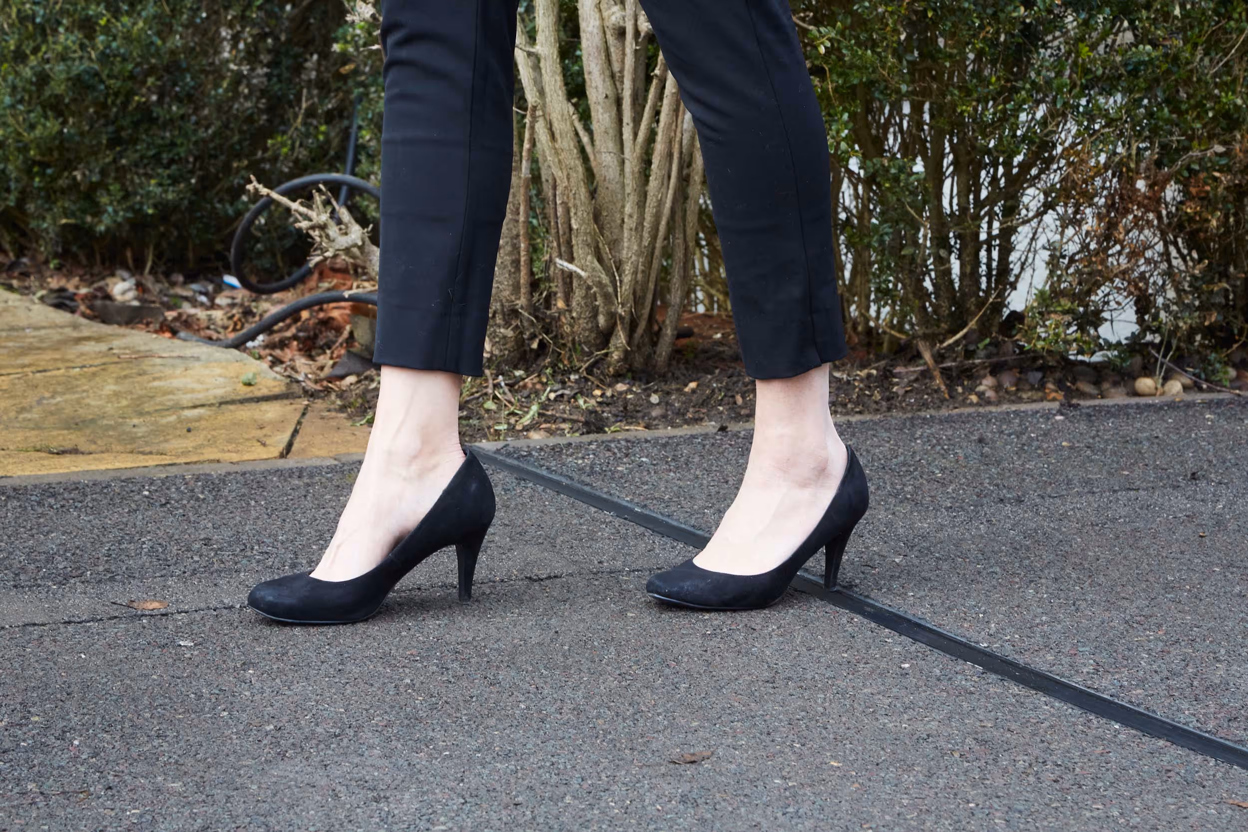 A person wearing black high heels walks on a paved path.