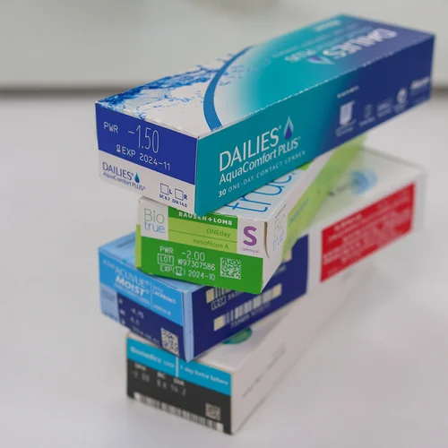 Stacked contact lens boxes in various colors and brands displayed