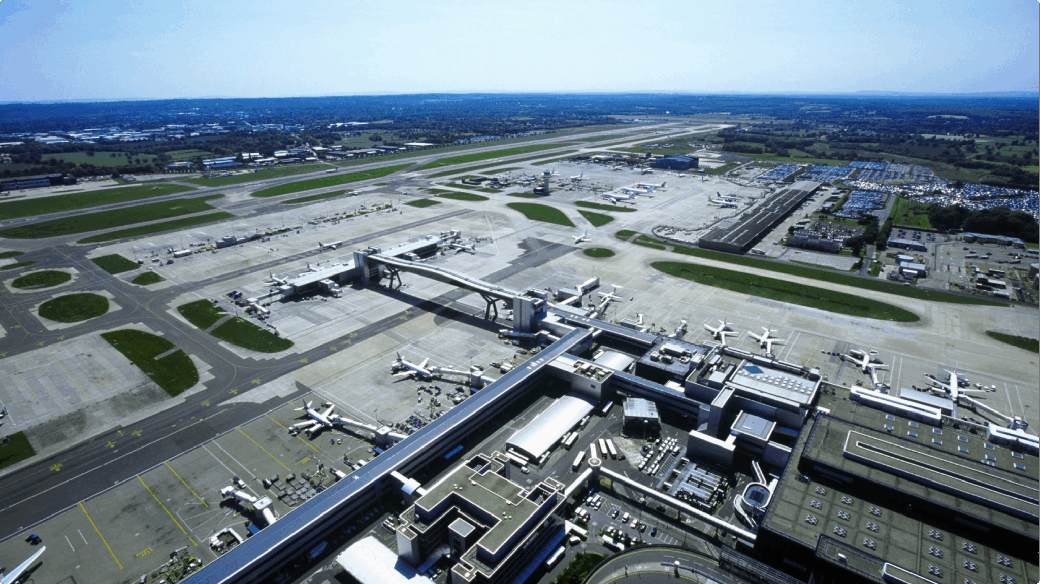 Aerial view of a large airport with multiple airplanes parked at gates, runways, taxiways, and surrounding buildings.