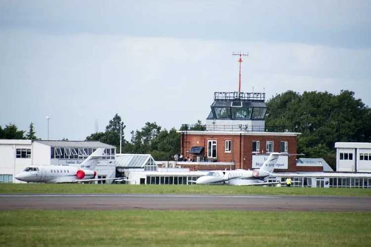 Two private jets parked near a small brick airport control tower and terminal buildings.