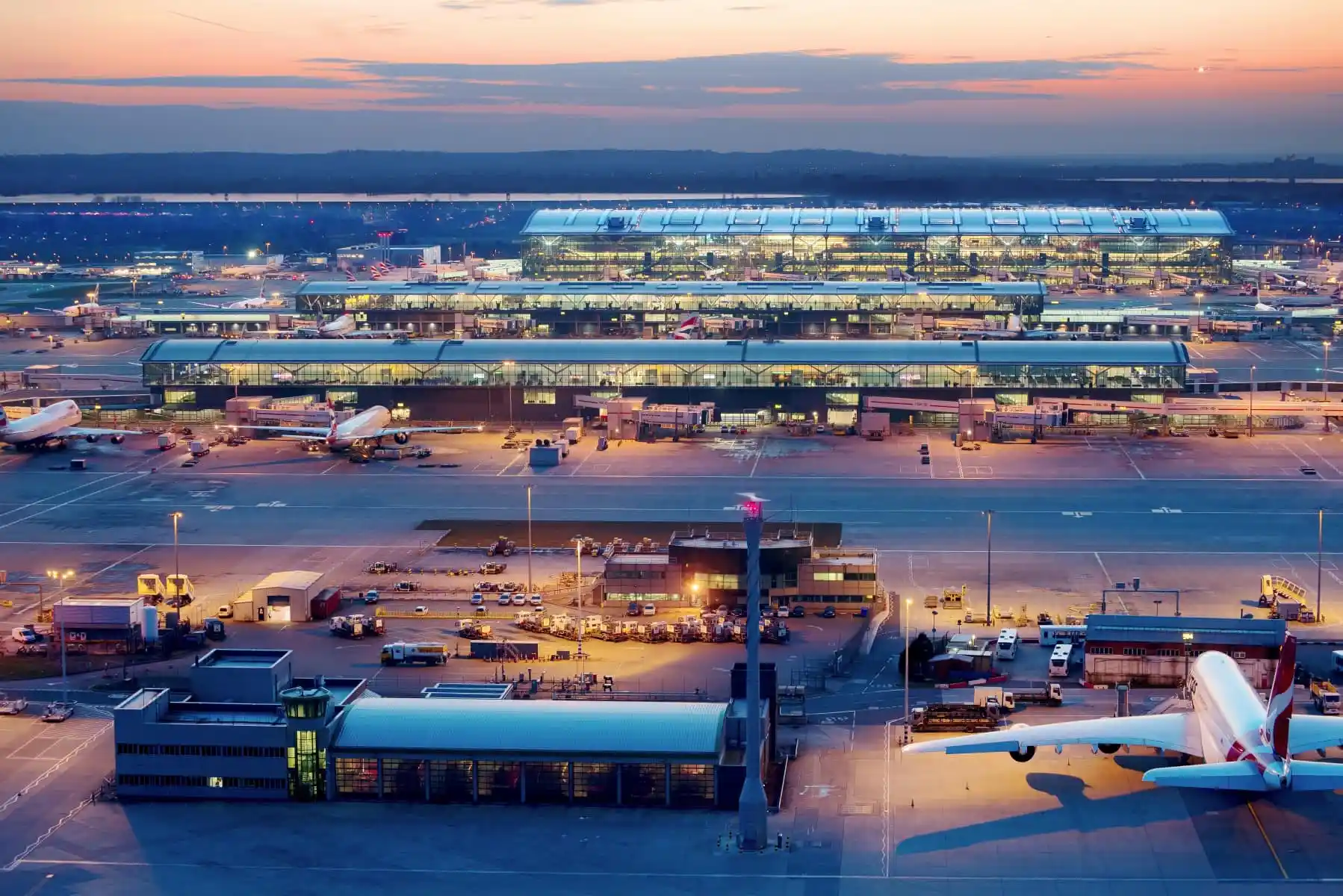 Aerial view of a large airport terminal with multiple airplanes parked at gates during sunset.