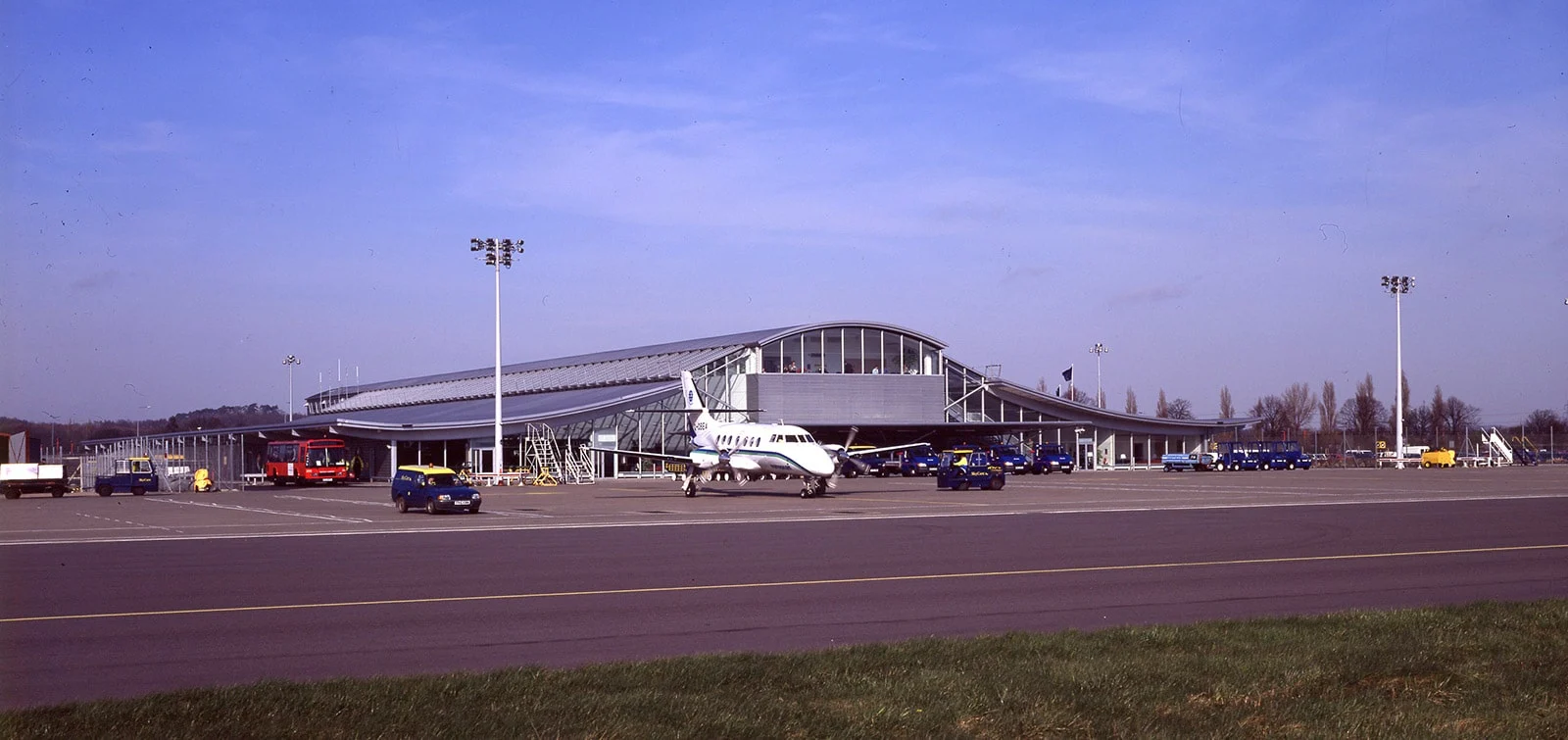 Small passenger airplane parked on the tarmac in front of a modern airport terminal building under a clear blue sky.