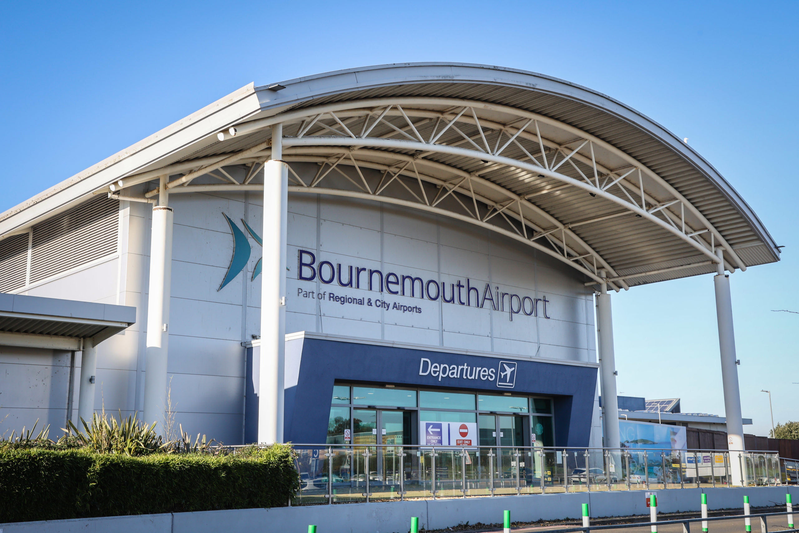 Exterior of Bournemouth Airport departures entrance with large curved roof and clear sky.