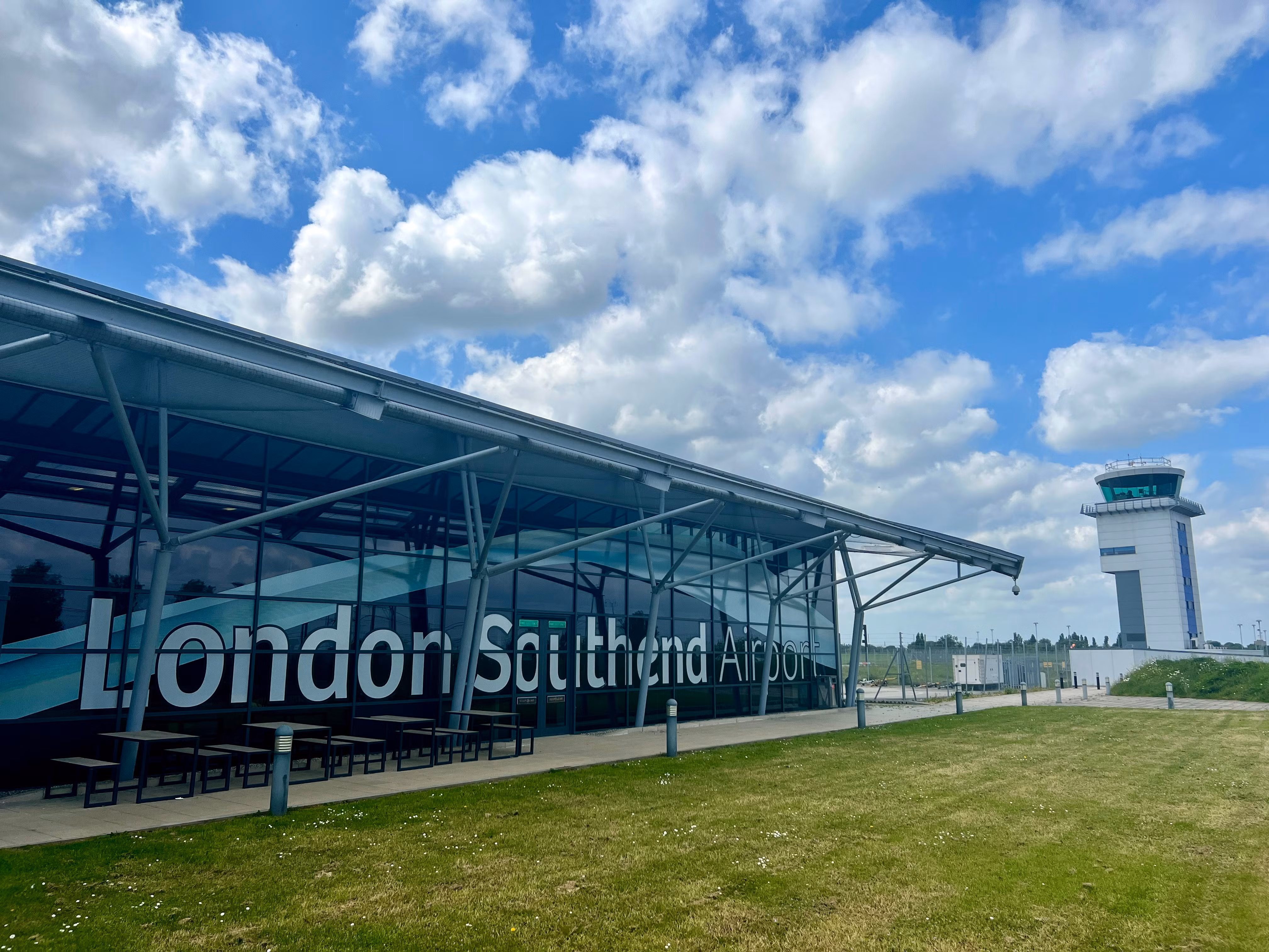 Modern London Southend Airport terminal building with large glass windows and control tower under a blue sky with scattered clouds.