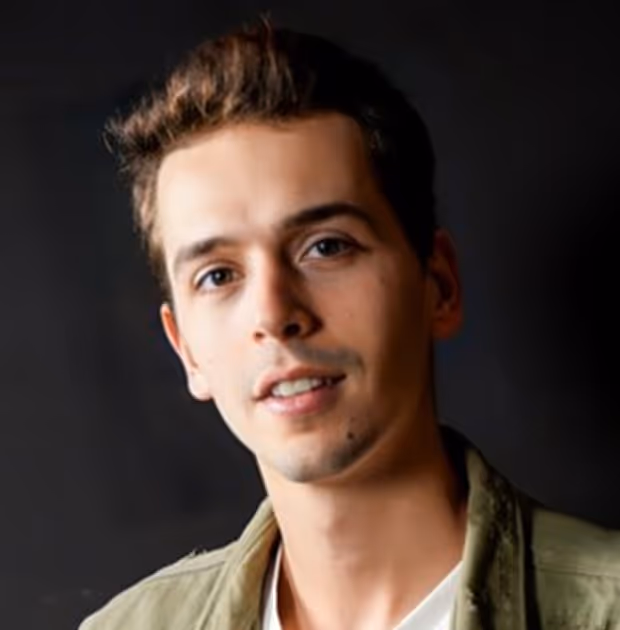 Portrait d'un jeune homme souriant avec une veste verte sur un fond sombre.