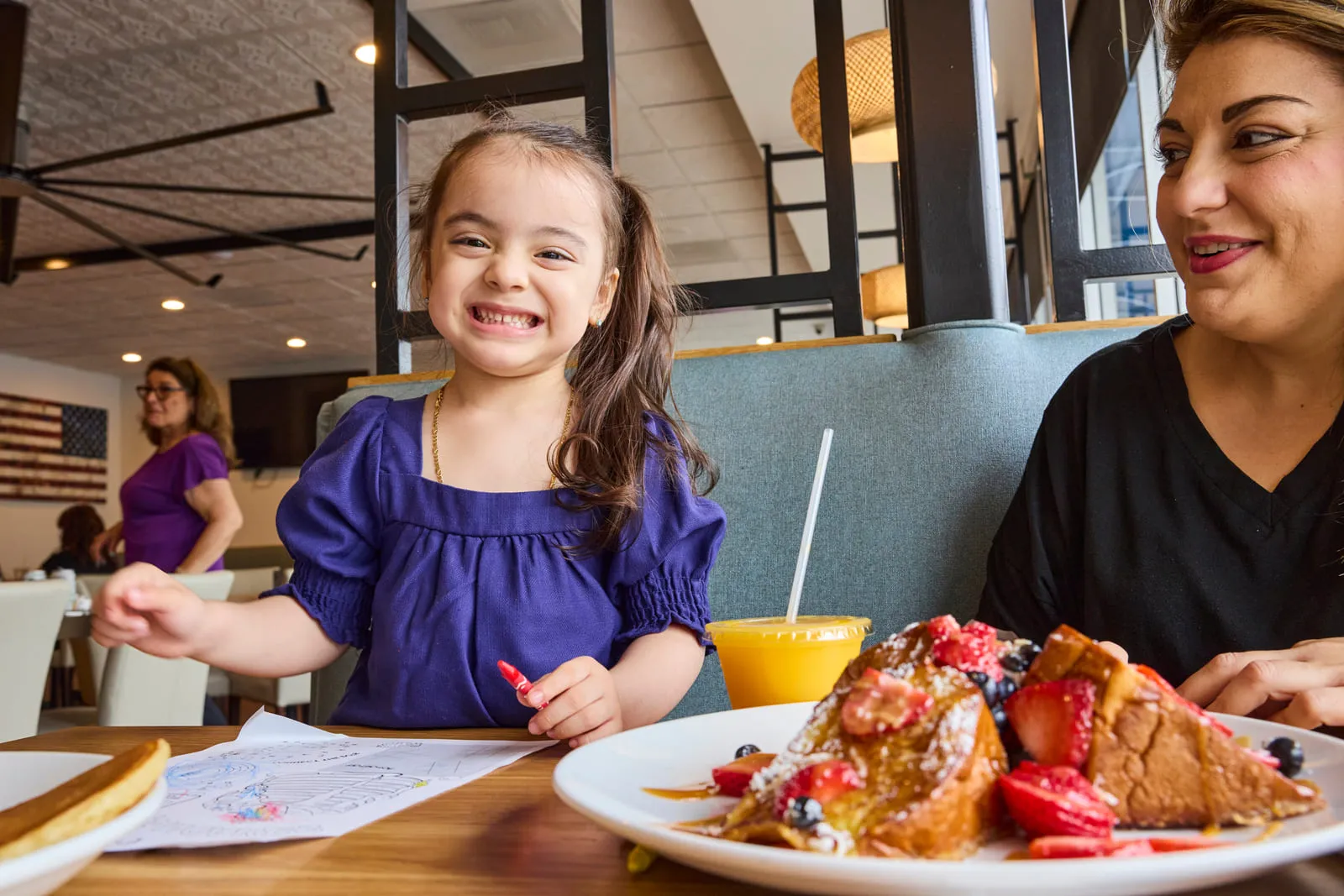Smiling child enjoying breakfast with parent at Broken Yolk Cafe