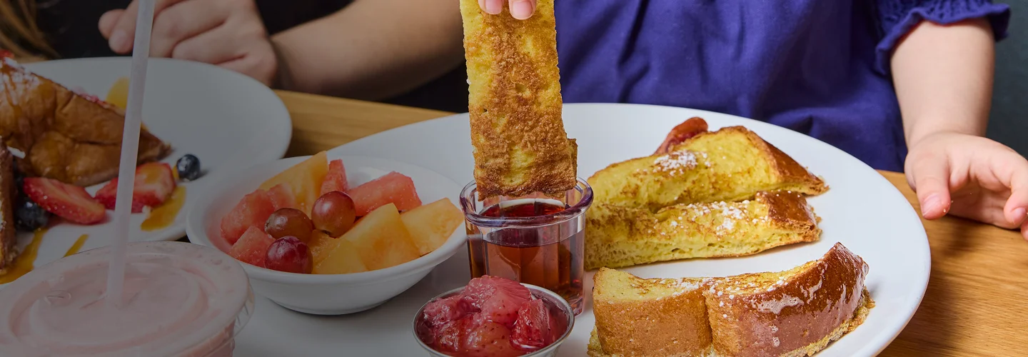 Little girl dunking french toast strips into syrup