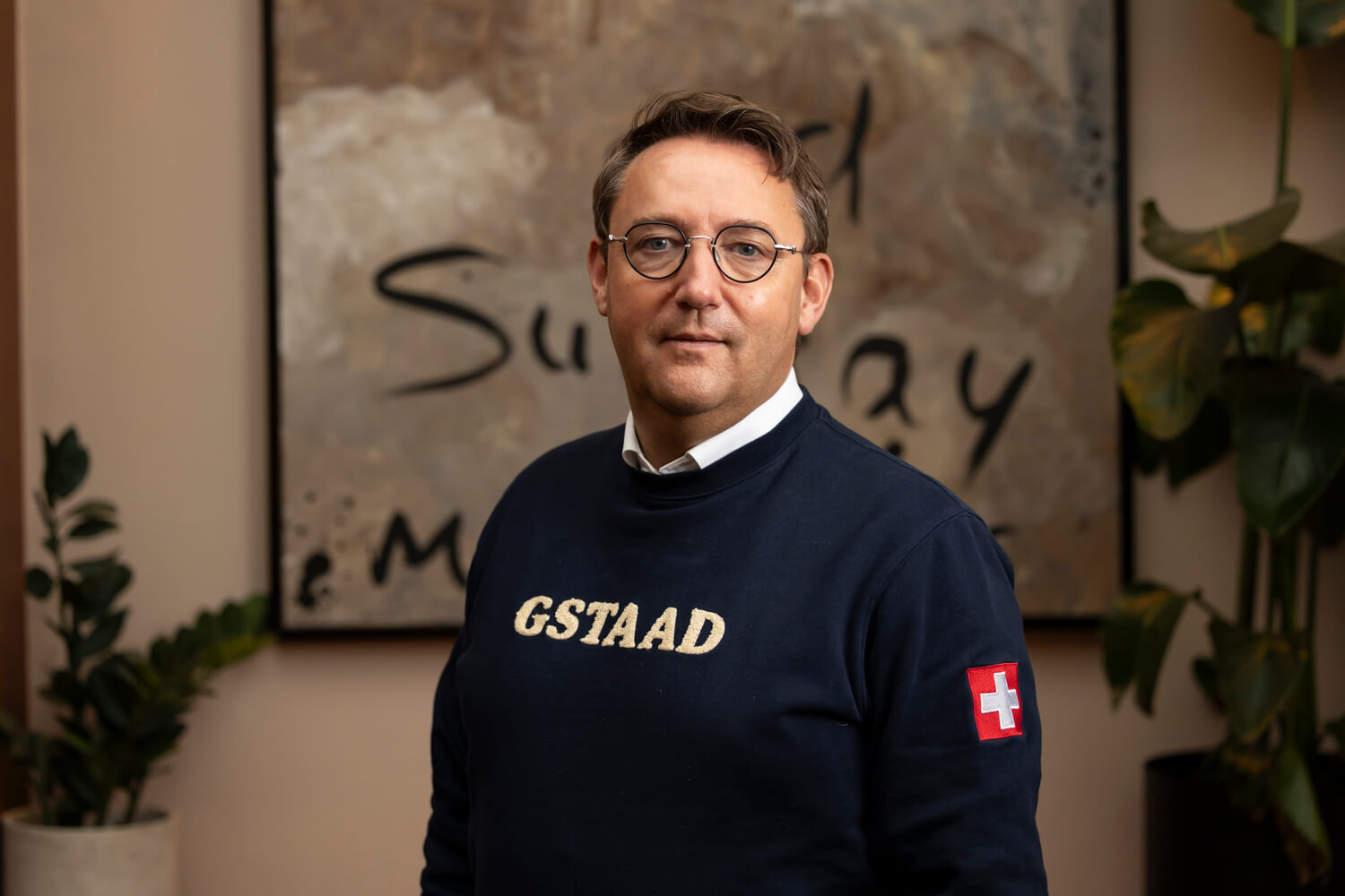 Michel Wichman vor einer Wand mit einem großen Bild und Pflanzen.